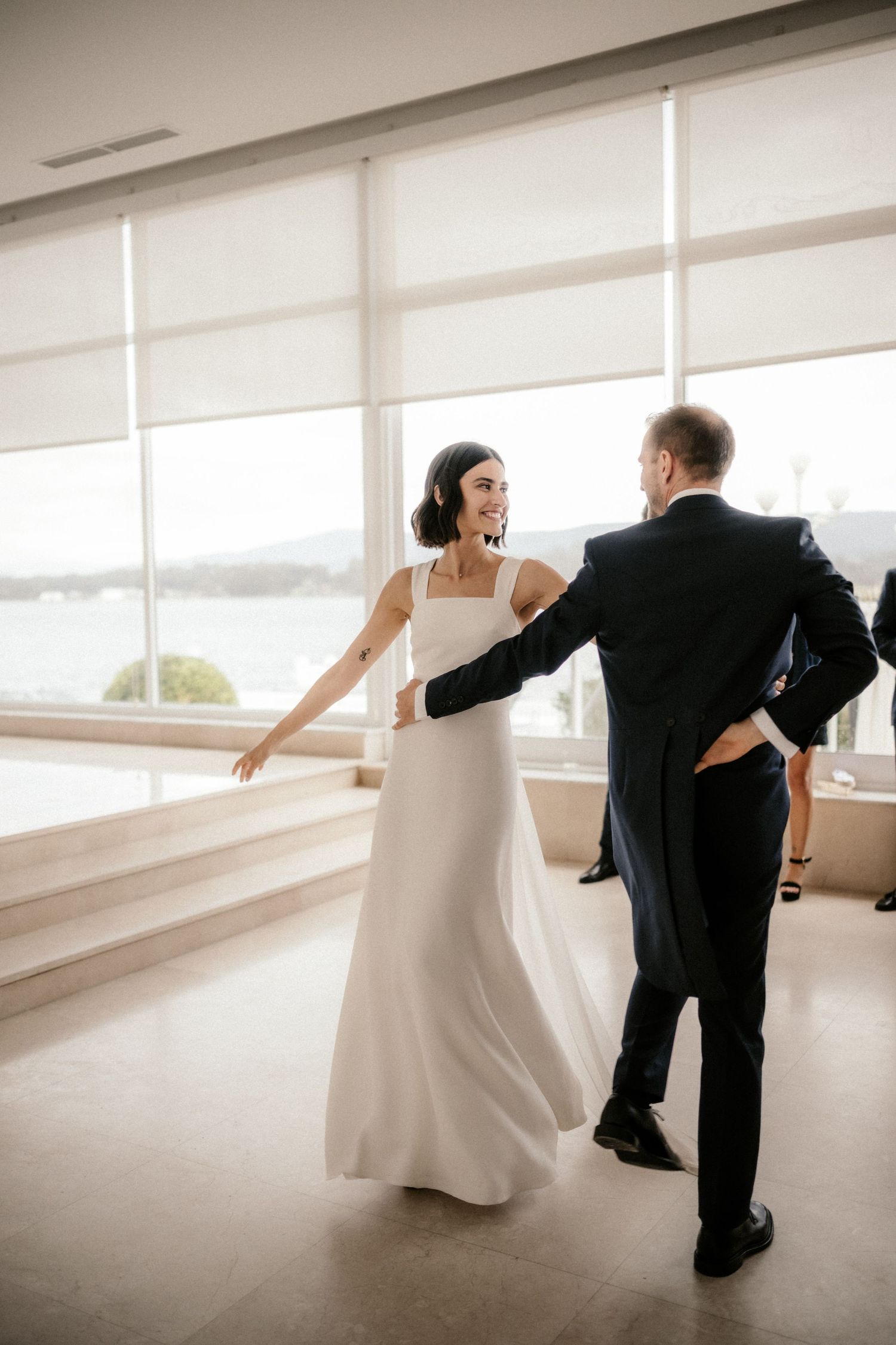 A sequence of five photos showing a bride and groom dancing together in a bright modern room with white roller shades.