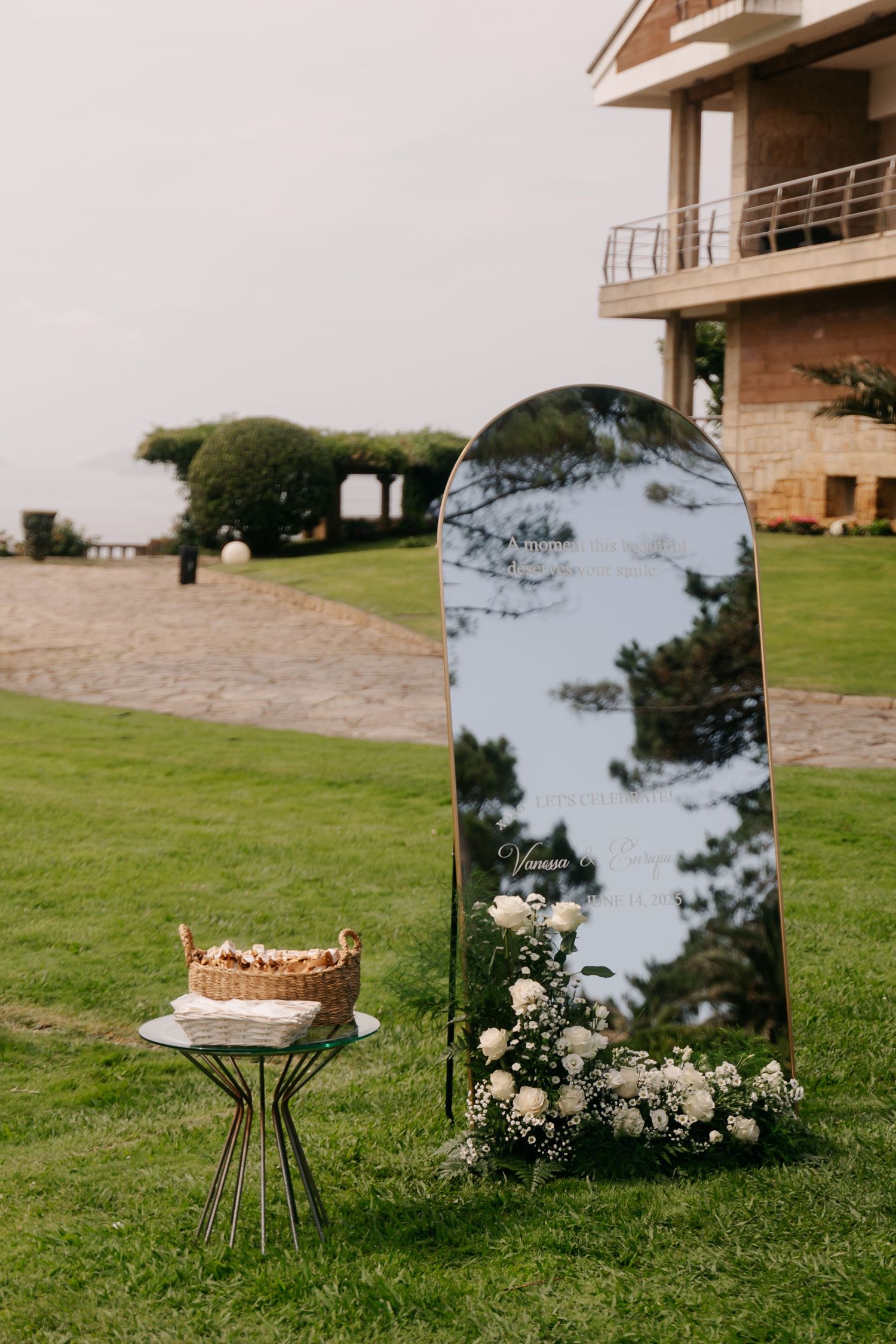Large decorative mirror and small table with floral arrangement set up on grass lawn for outdoor wedding ceremony.