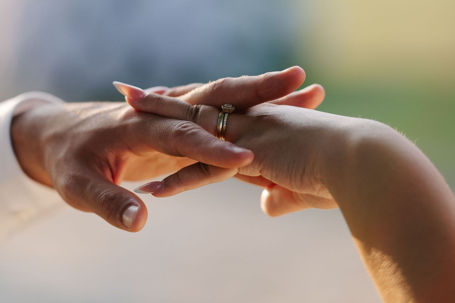 Close-up of hands touching gently with engagement ring in soft natural light.