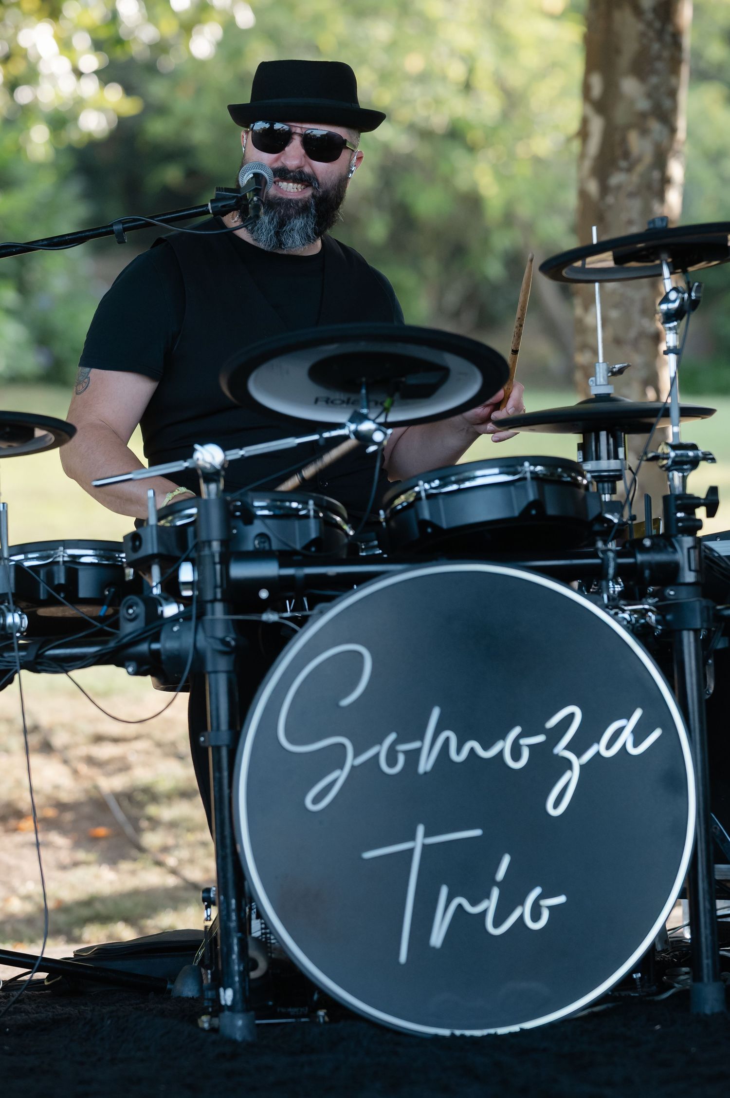 Black drum set with custom text written on bass drum heads in an outdoor setting.