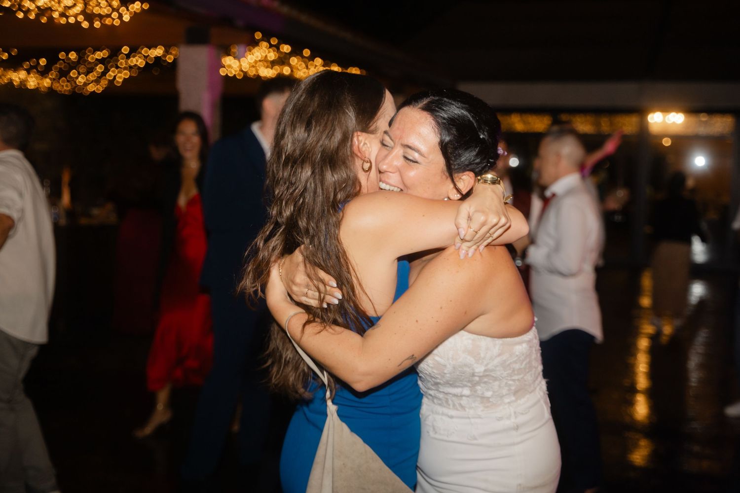 Wedding guests dancing and celebrating on a dimly lit dance floor with warm string lights overhead.