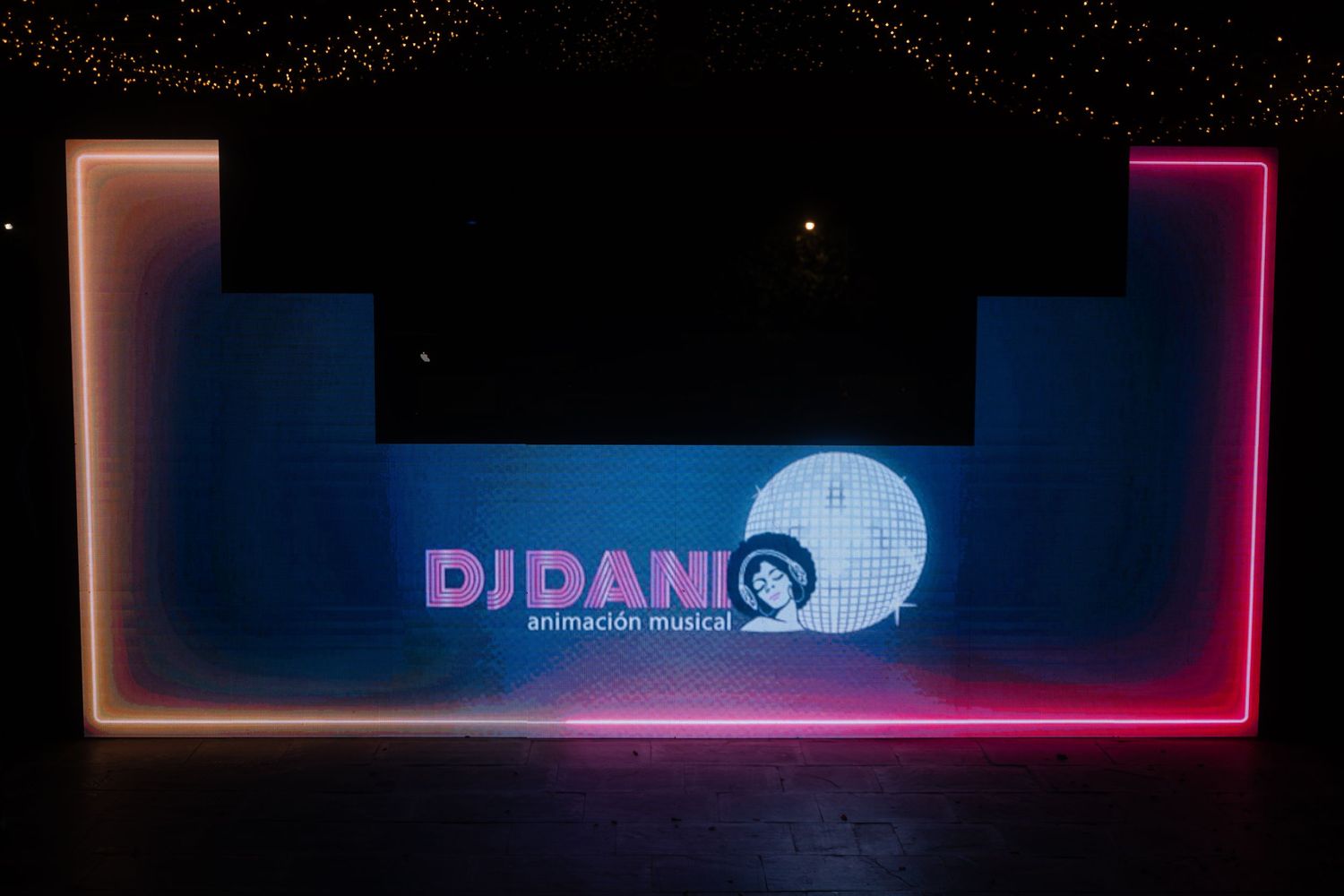 Neon pink and blue DJ booth illuminated in dark nightclub setting with glowing signage and equipment.