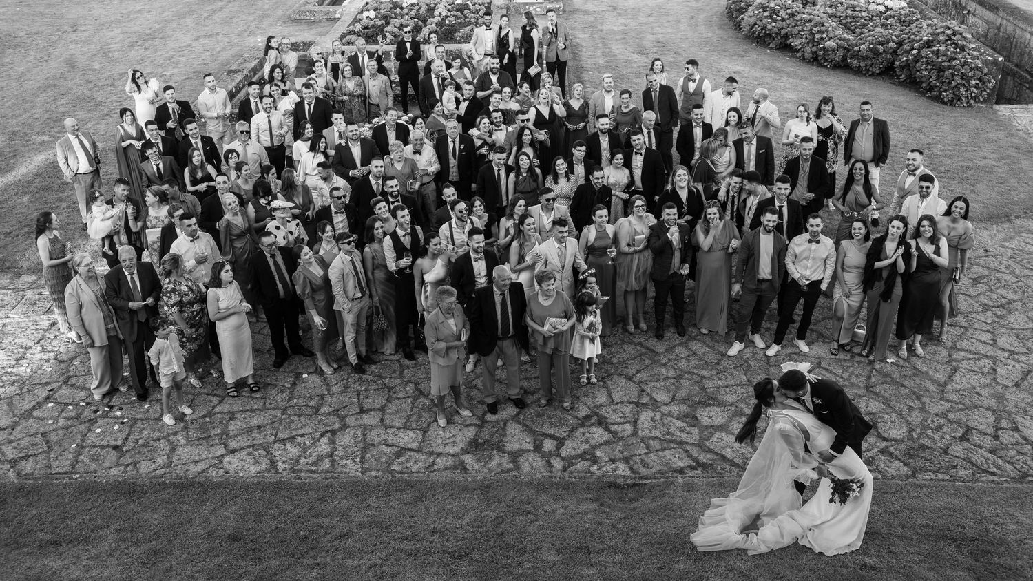 A black and white panoramic photograph shows a large group of people gathered outdoors for a formal event.