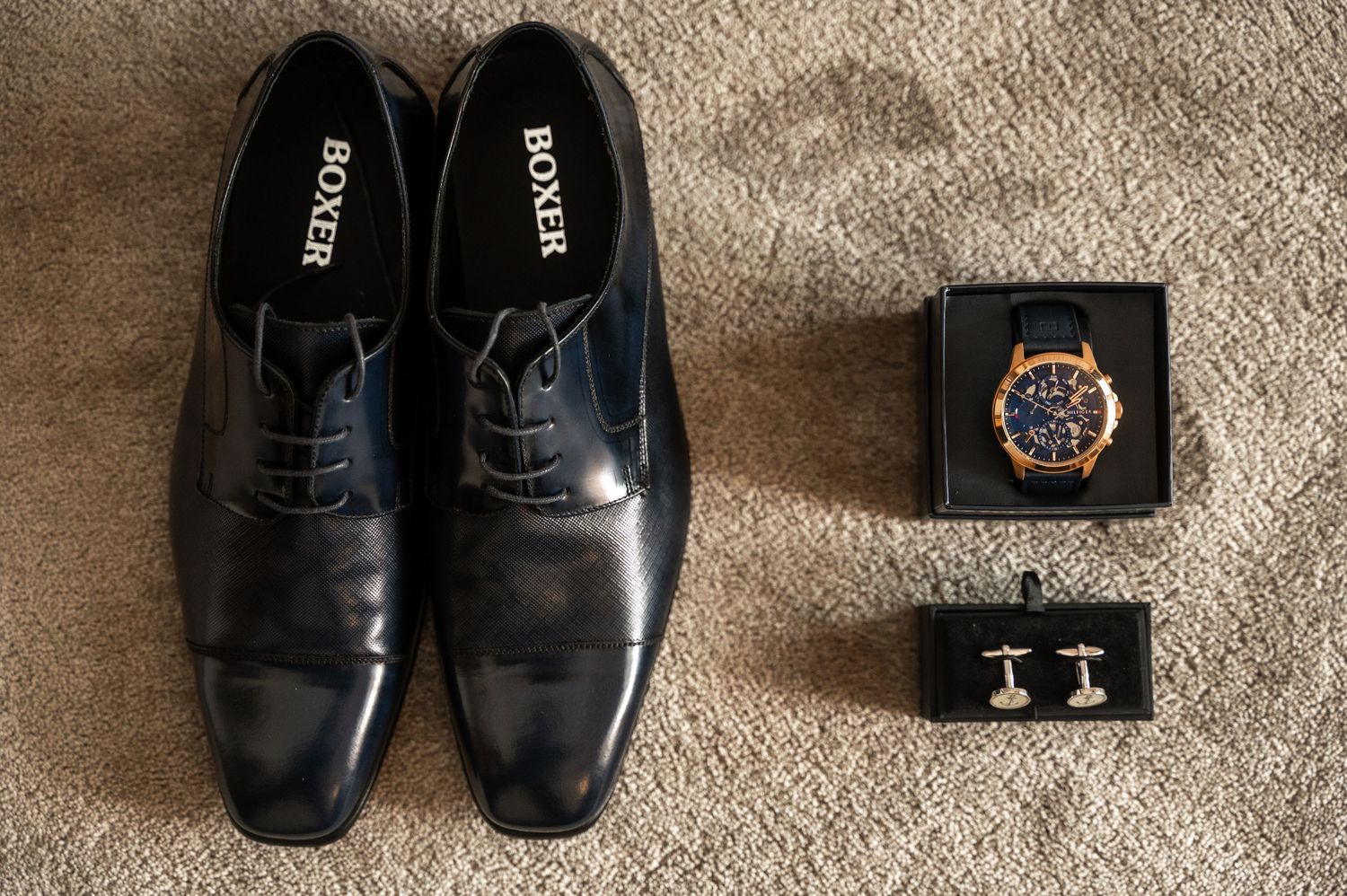 A collage of black leather dress shoes and accessories including cufflinks and a watch displayed on beige carpet.