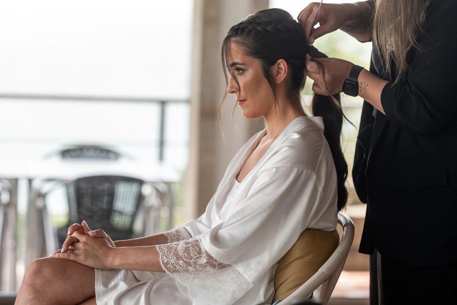 Professional makeup artist applies cosmetics to bride getting ready on her wedding day in bright indoor setting.