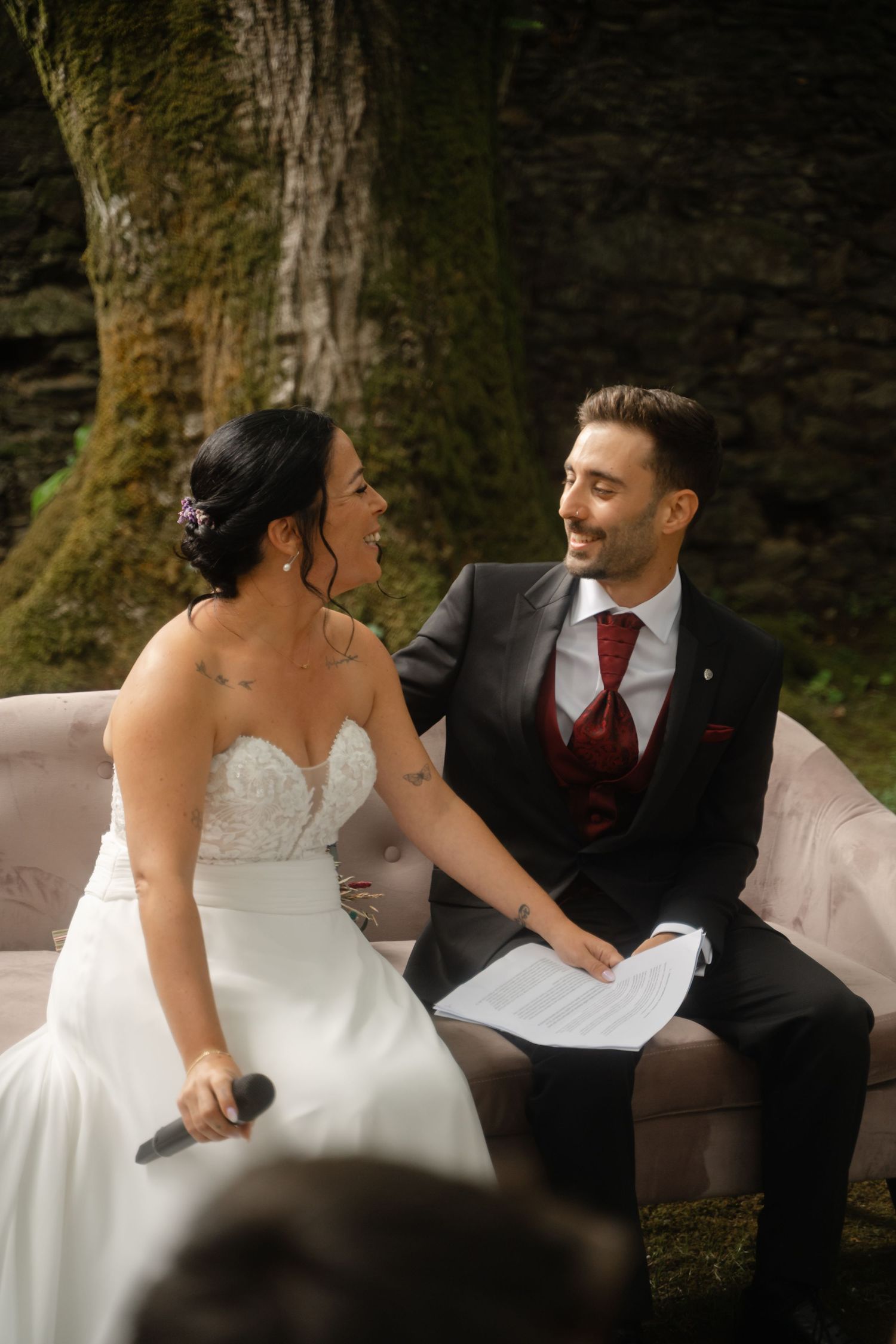 Wedding couple sits together on an outdoor couch sharing tender moments during their photoshoot.