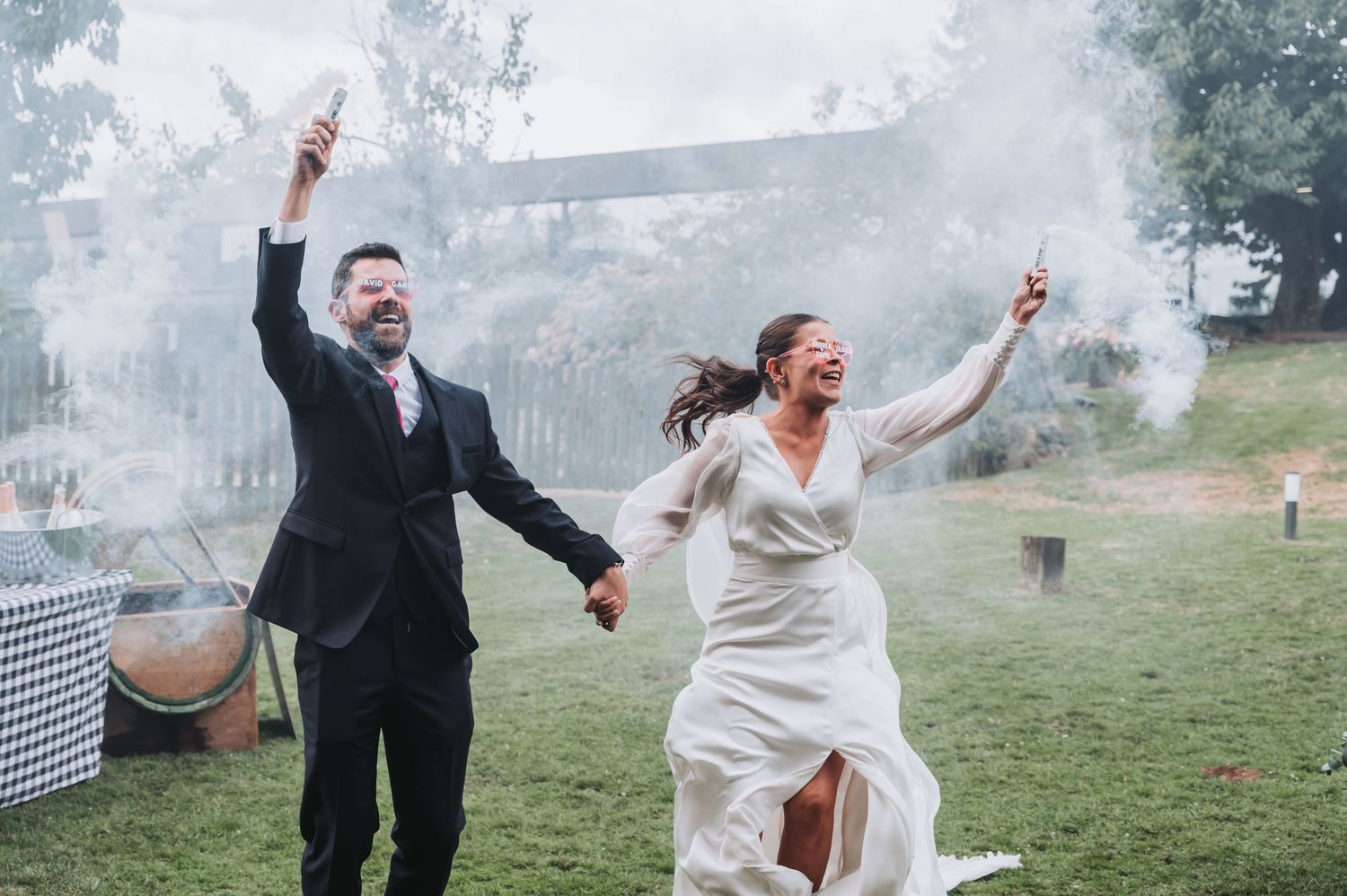 A couple celebrates joyfully in a misty outdoor setting with smoke effects during their wedding photoshoot.