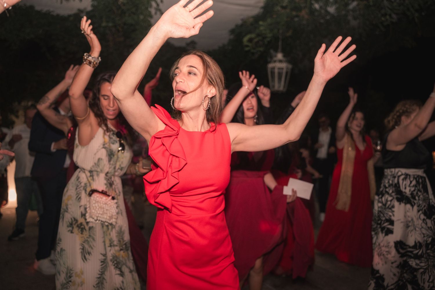 A group of people dancing together at a party with someone in a bright red dress moving energetically.