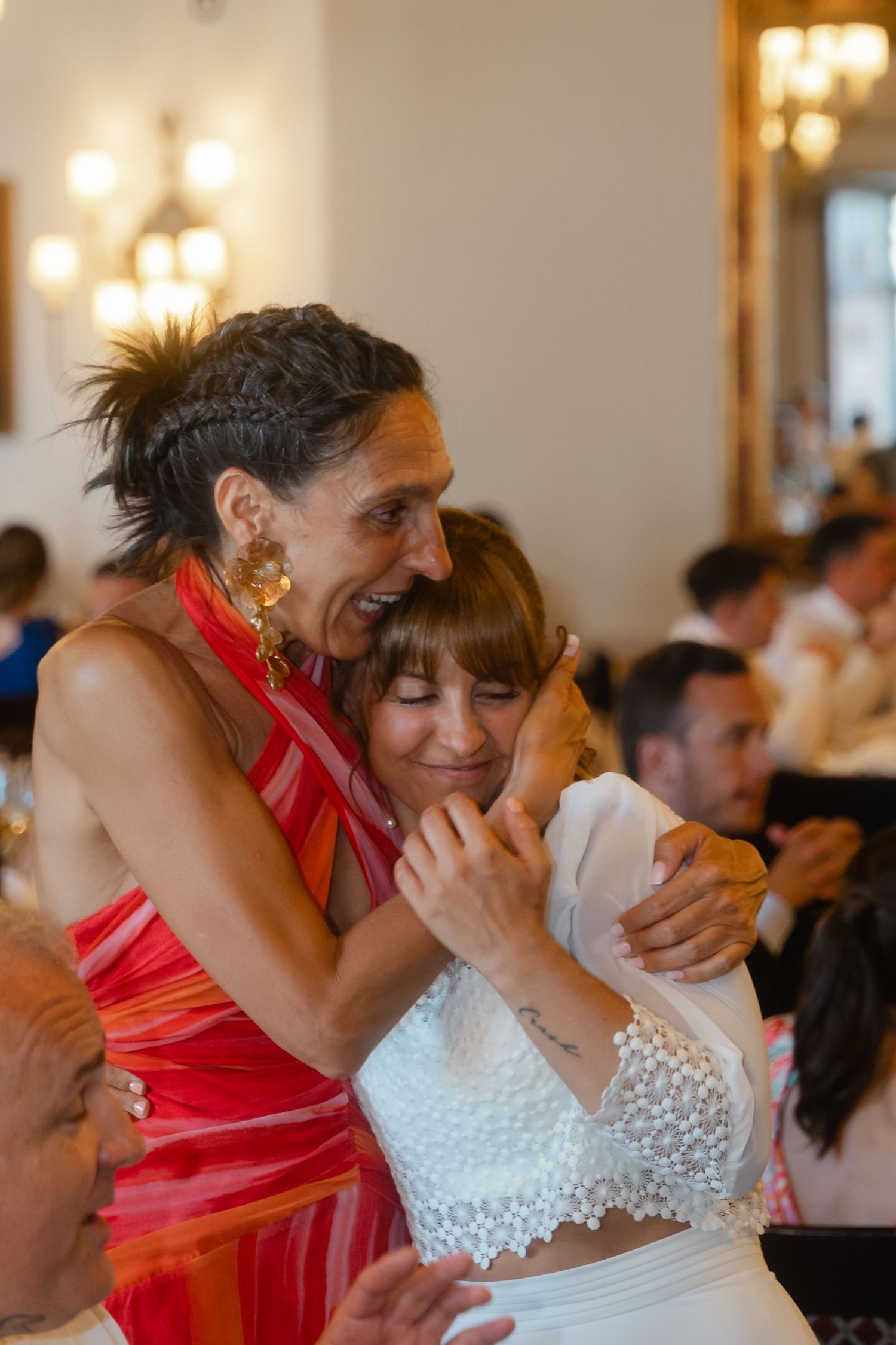 Two guests share an emotional embrace during a wedding celebration with warm lighting in the background.