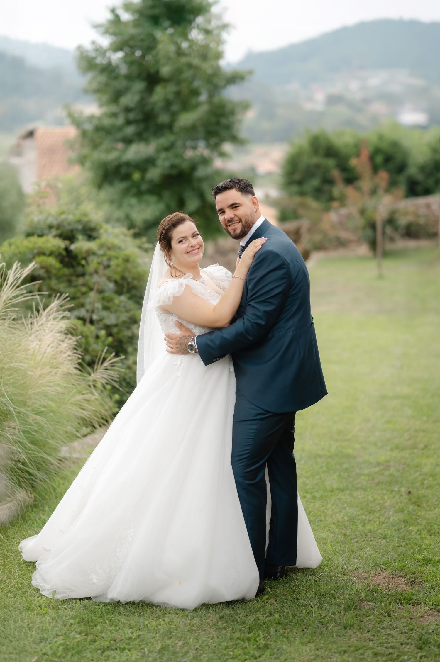A couple in wedding attire dancing together on a grassy hillside with mountains in the background.
