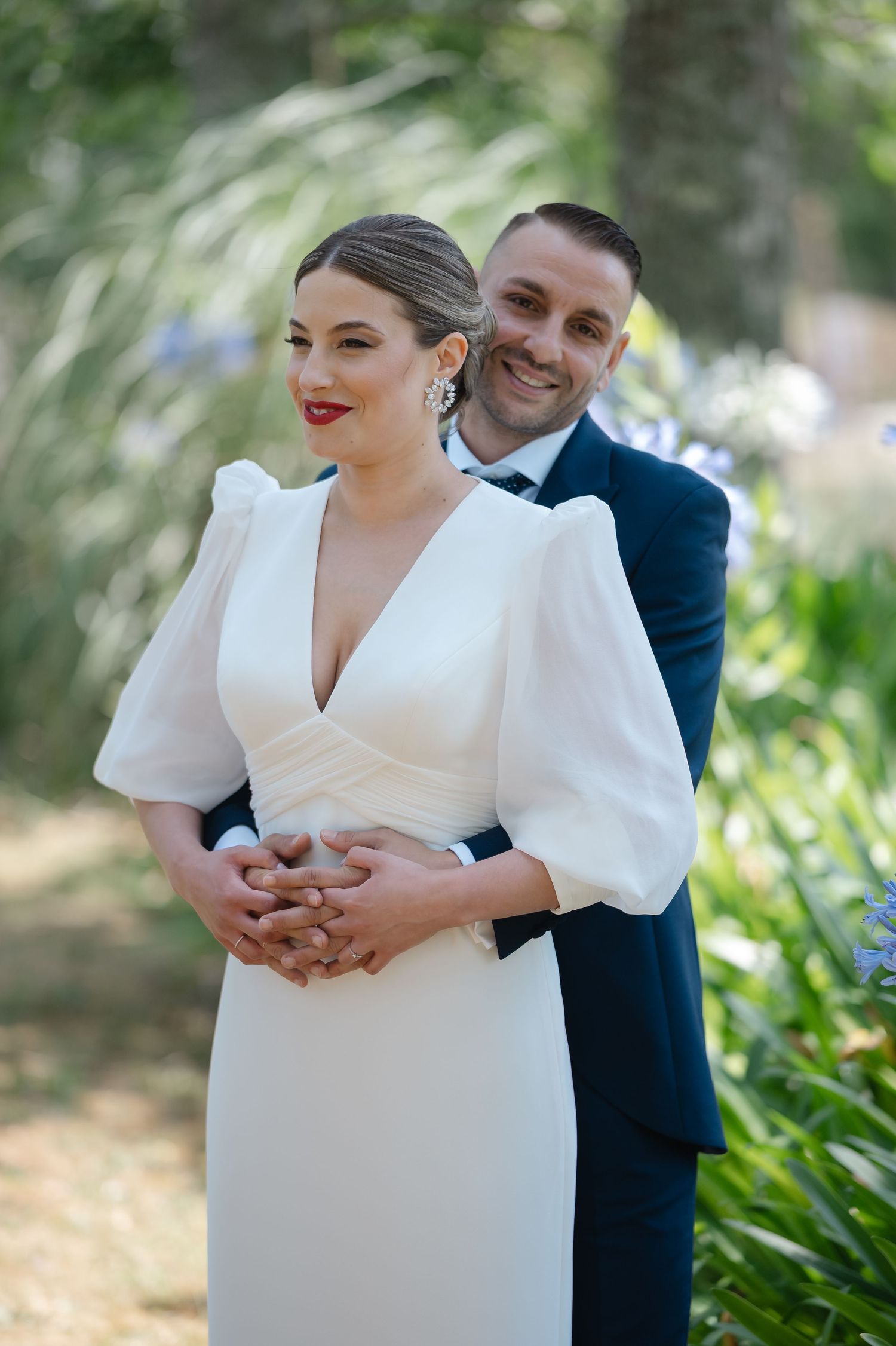 Wedding couple poses in garden setting with bride wearing modern white dress with puff sleeves.