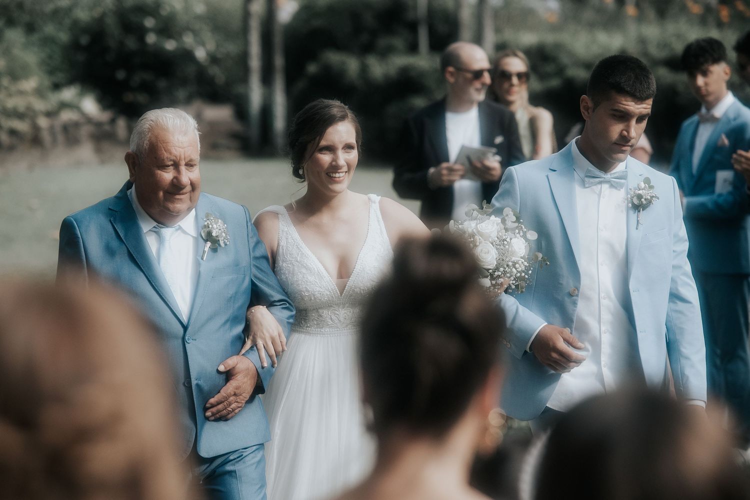 A wedding ceremony processional with people walking down the aisle, with attendees in light blue and white attire.
