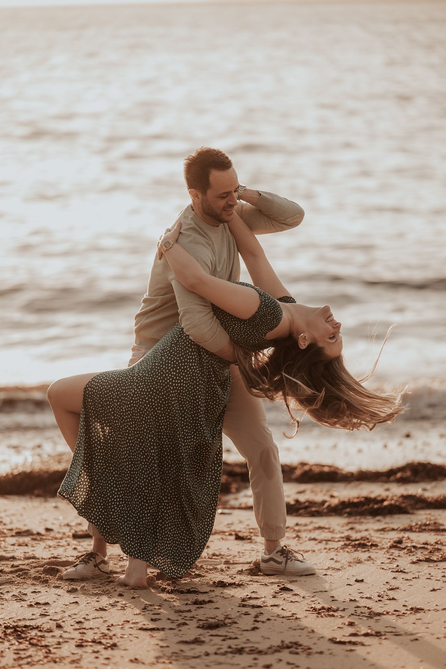 Couple sitting together on a sandy beach at sunset in casual attire.