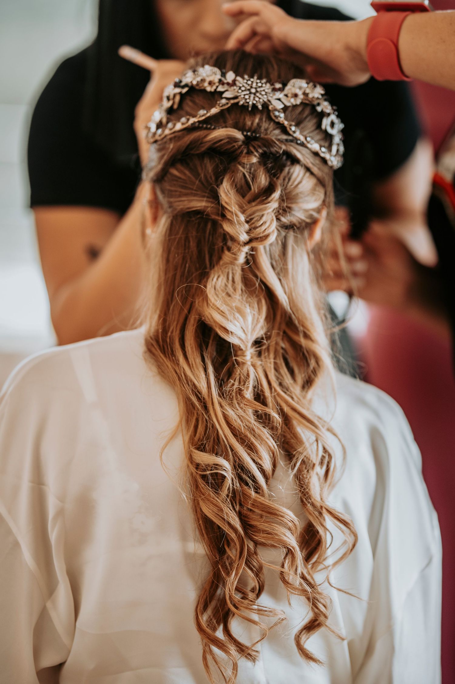 Close-up of elegant bridal hairstyle with braids, curls and crystal hair accessories in white robe.
