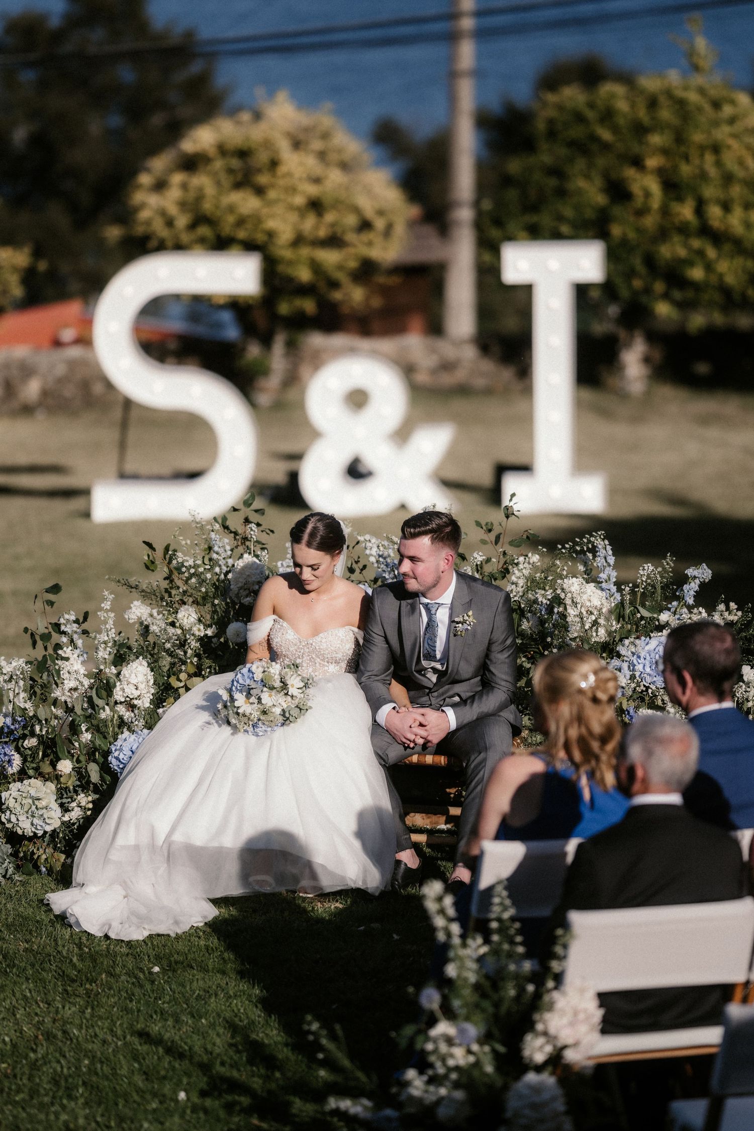 A wedding ceremony outdoors with large decorative S&T letters and white floral arrangements.