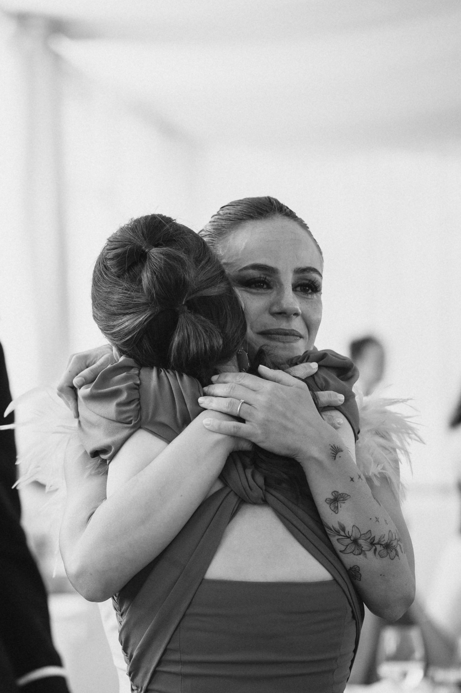 Black and white photo captures emotional embraces between wedding guests during reception.