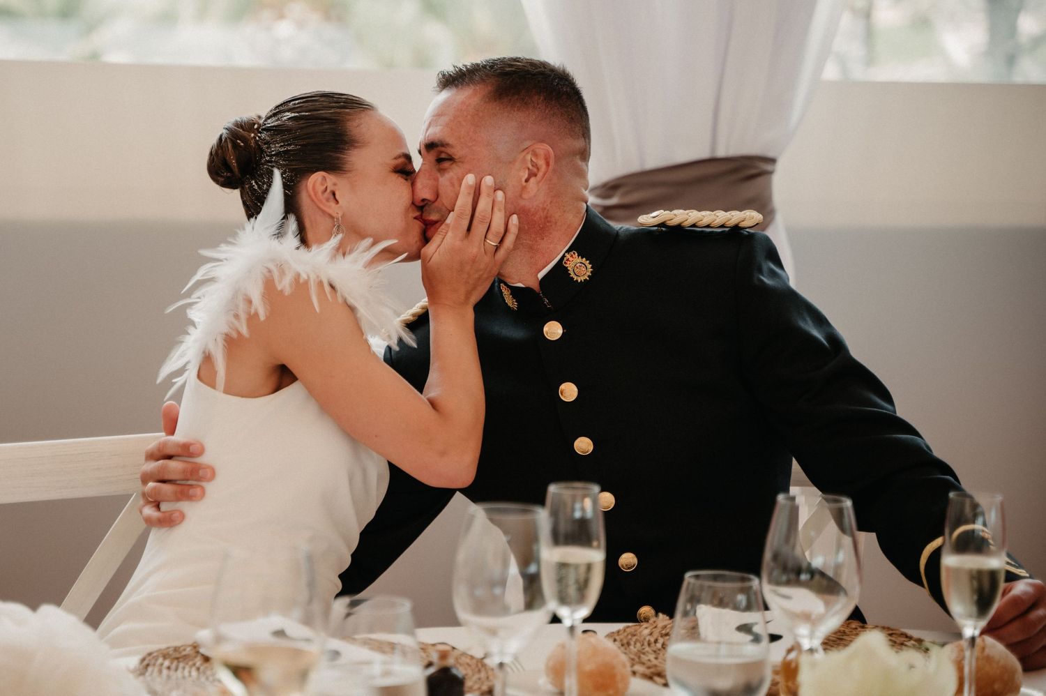 A couple shares a romantic kiss at their wedding reception with elegant table settings in the background.