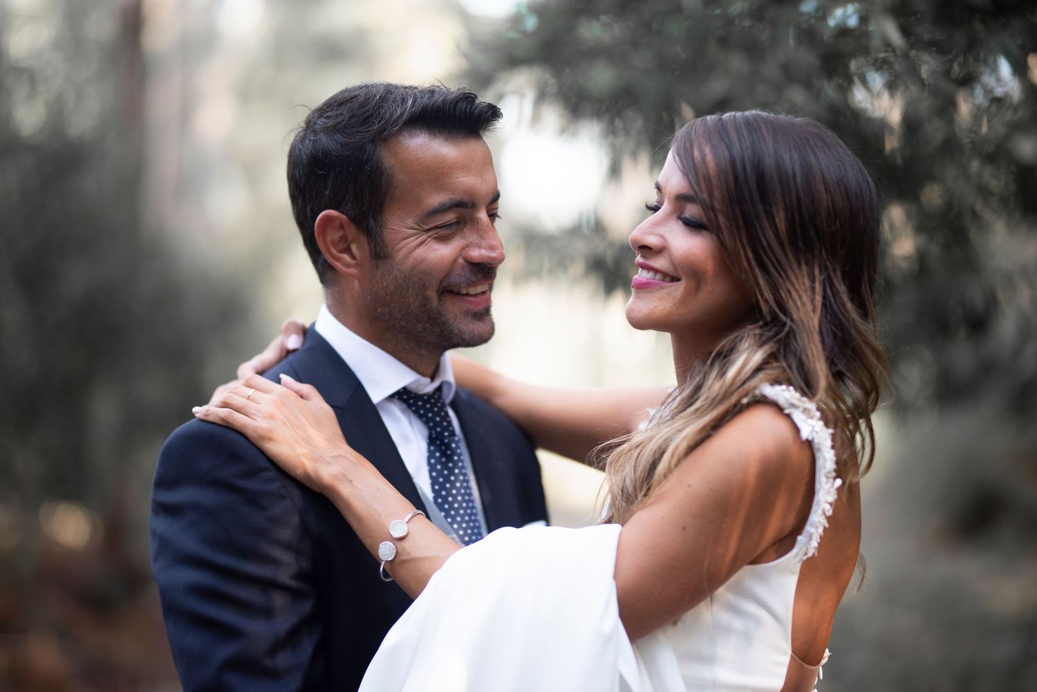 A happy couple in wedding attire embrace and laugh together during an outdoor photo session.