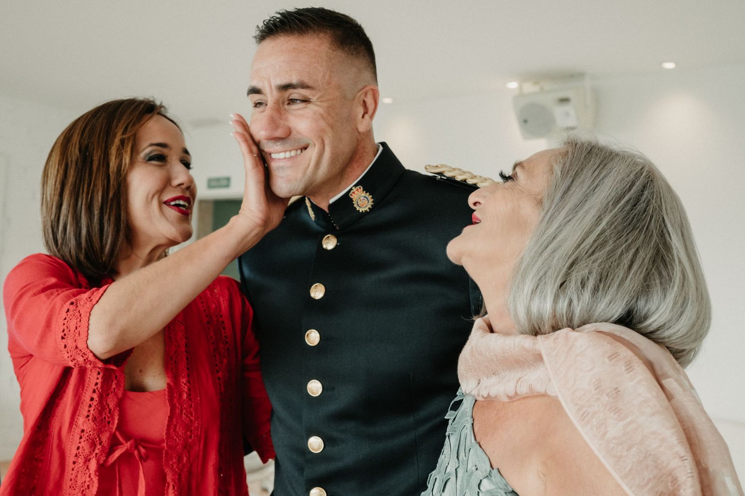 Three people share a joyful moment together, with one wearing a formal military dress uniform with brass buttons.