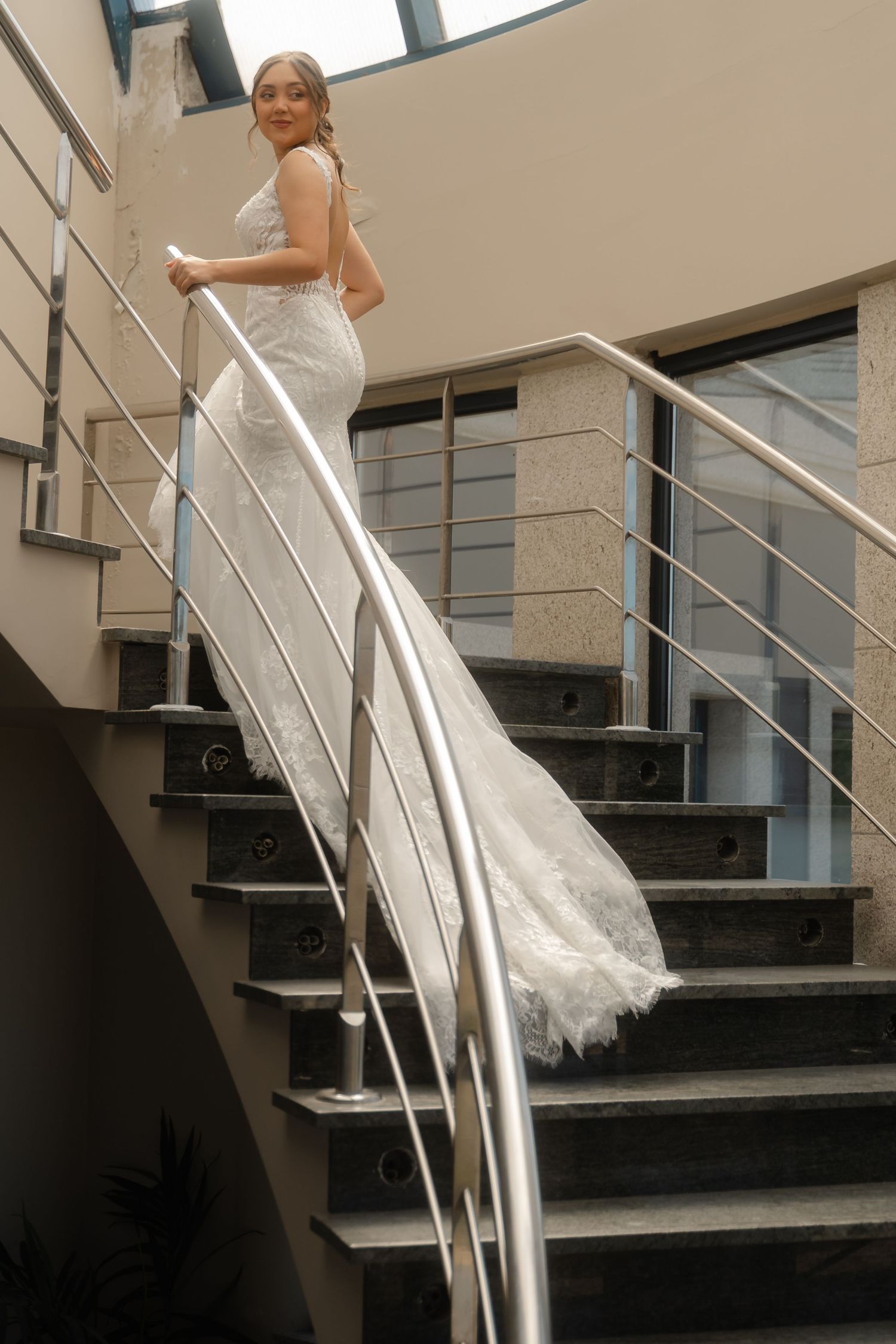 A person in a white wedding dress gracefully descends a modern staircase with glass railings in a sequence of photos.