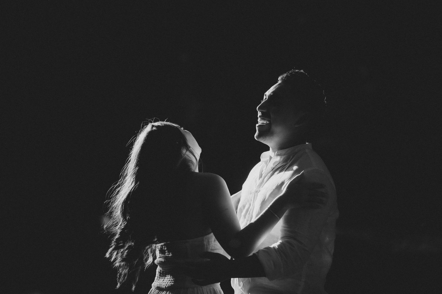 Romantic couple in black and white silhouette embracing against dark background.