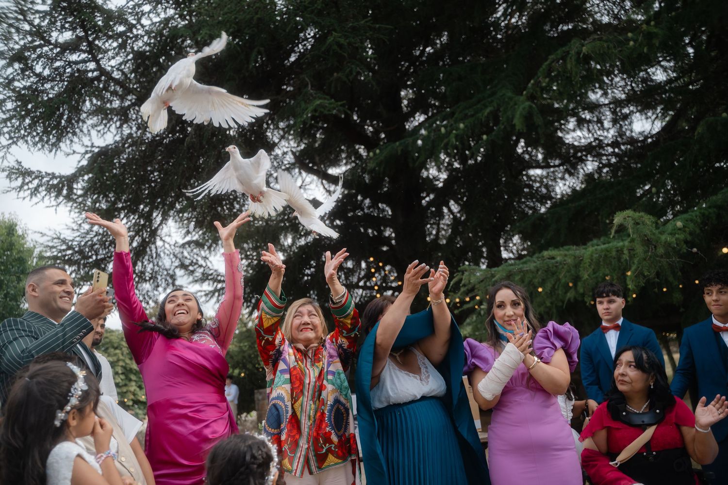 White doves being released into the sky during an outdoor wedding celebration as guests cheer.