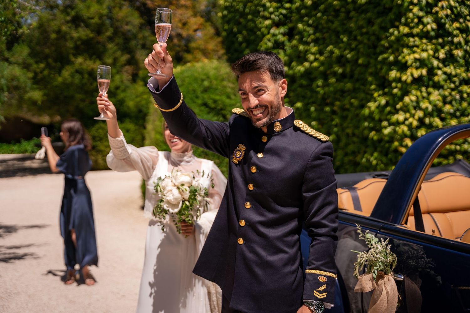 Celebratory group toasting with champagne glasses outdoors in formal attire at a sunny garden event.