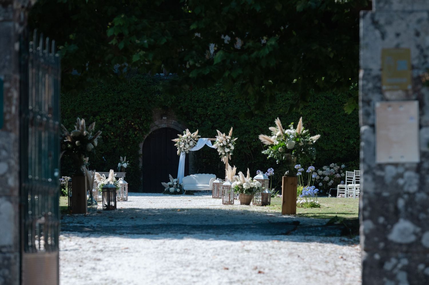 White floral arrangements adorn tables at an outdoor garden wedding reception with string lights overhead.