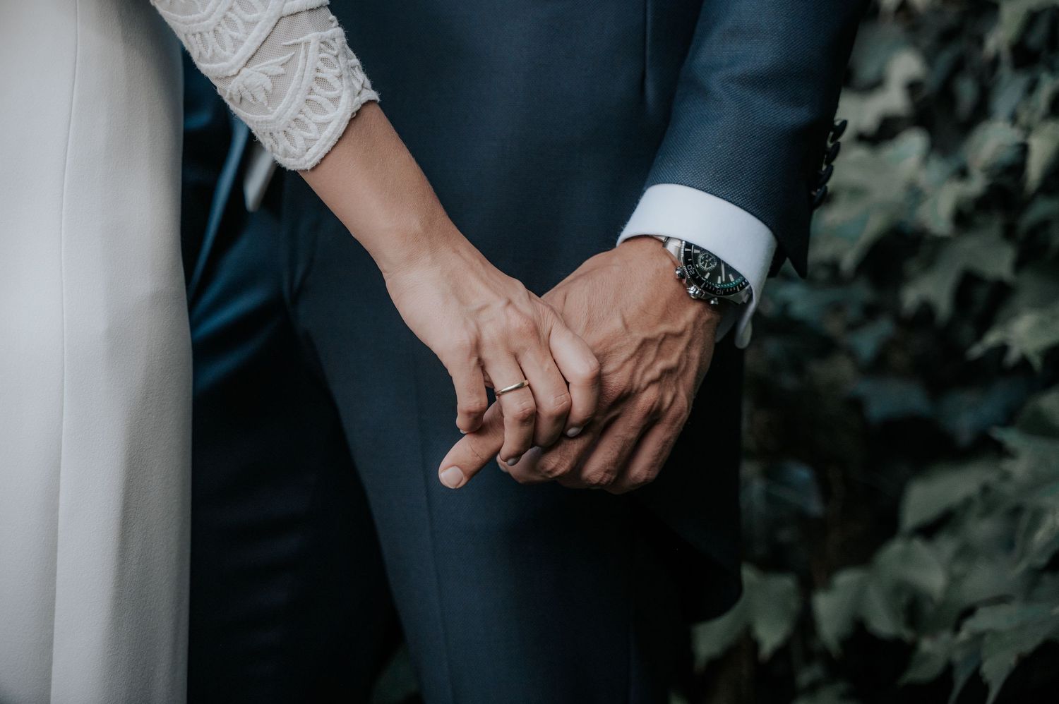 A couple in formal attire holds hands against a white column backdrop.