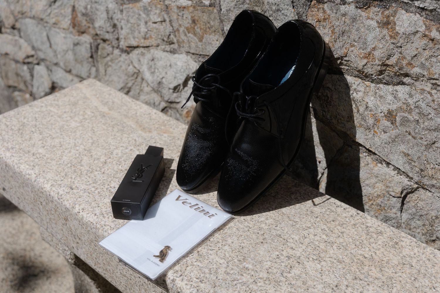 A black dog wearing a service vest lies on a stone floor next to paperwork and shoes.