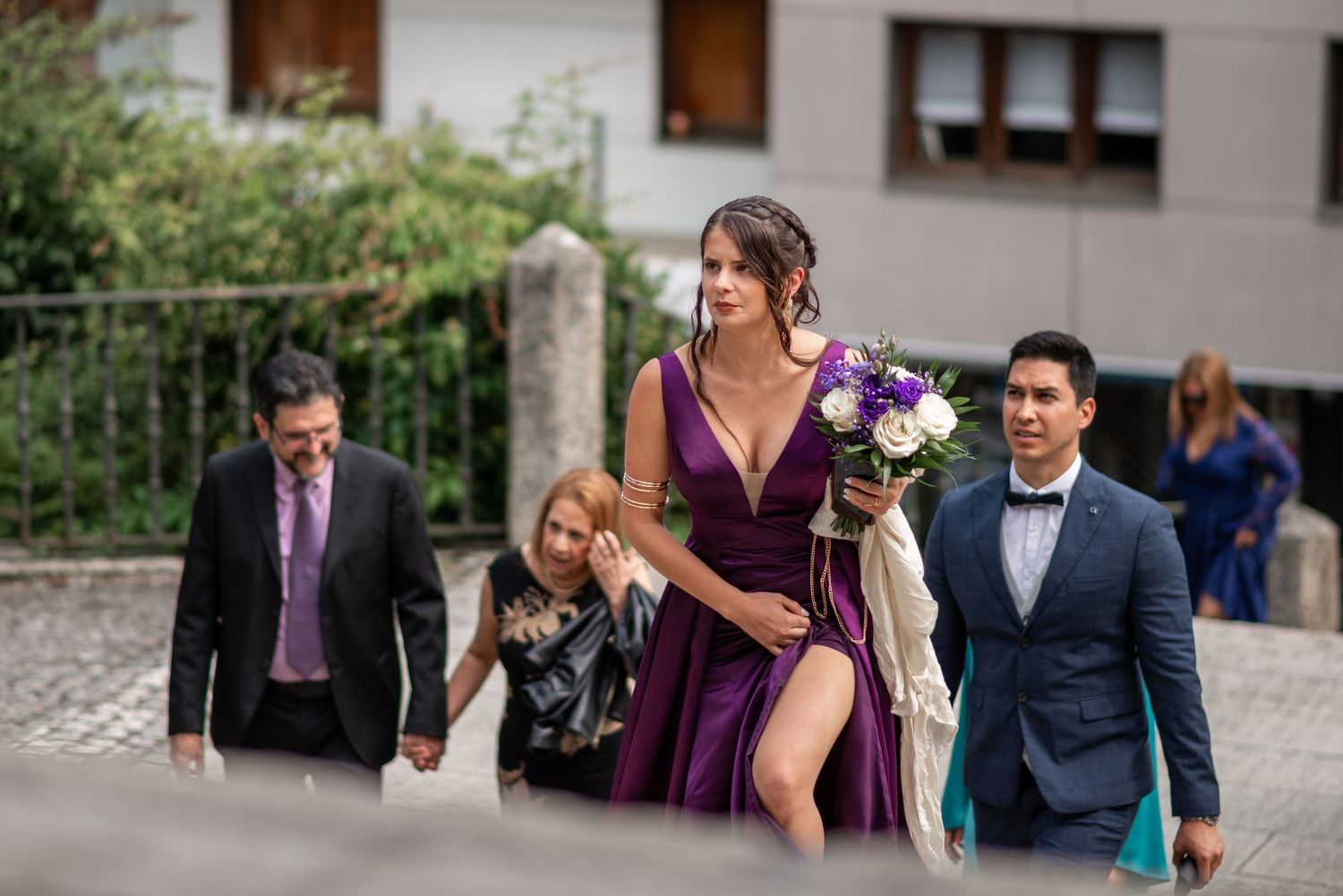 Wedding party members in purple dresses and suits walk together outdoors.