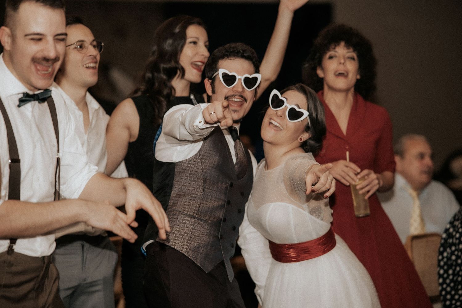 Wedding guests dance and celebrate joyfully on the dance floor at an indoor reception party.