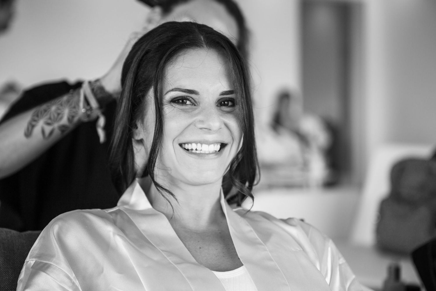 A black and white portrait of a smiling person in a white robe getting ready for their wedding day.