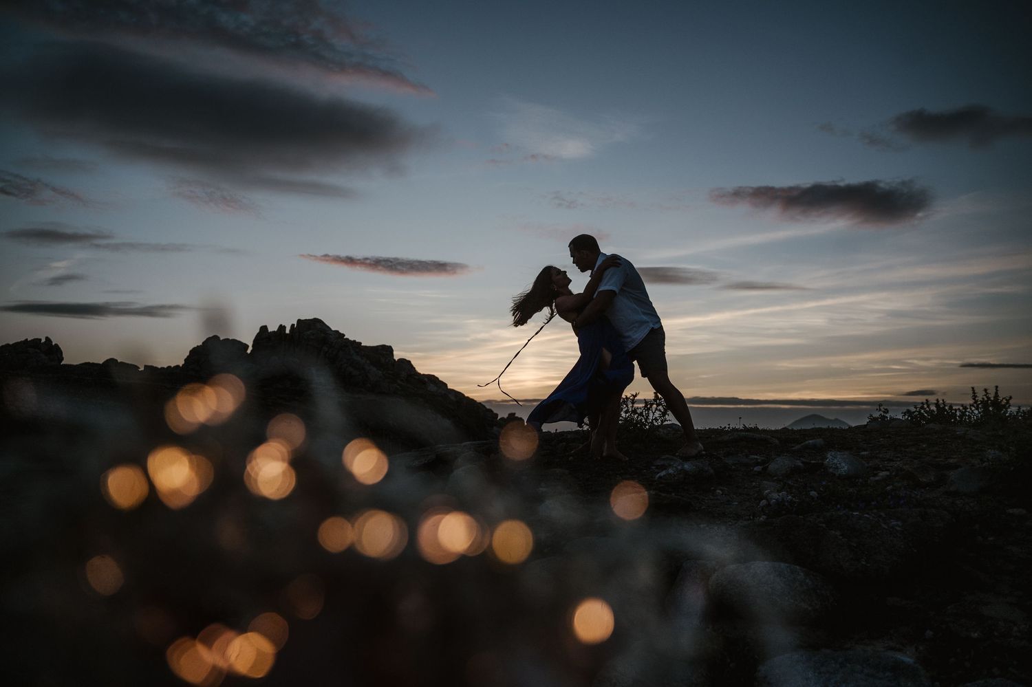 Silhouetted figure photographing at sunset with bokeh lights in foreground creating magical atmosphere.