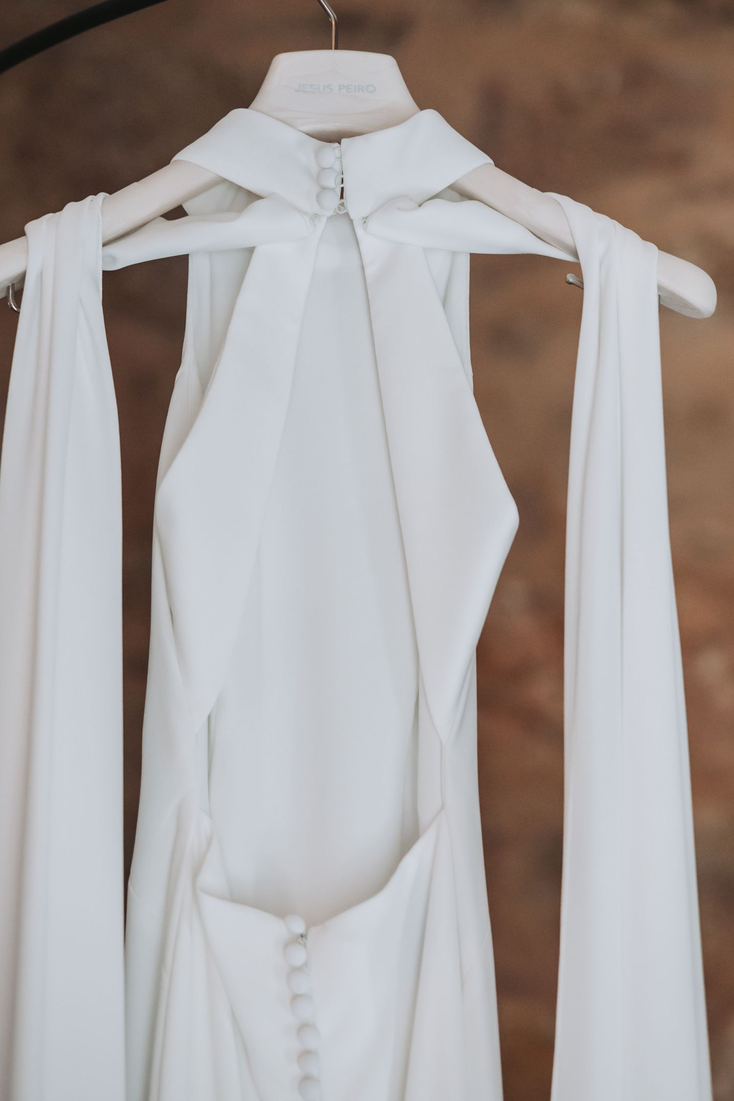 Row of white wedding dresses hanging on hangers against a brown background.