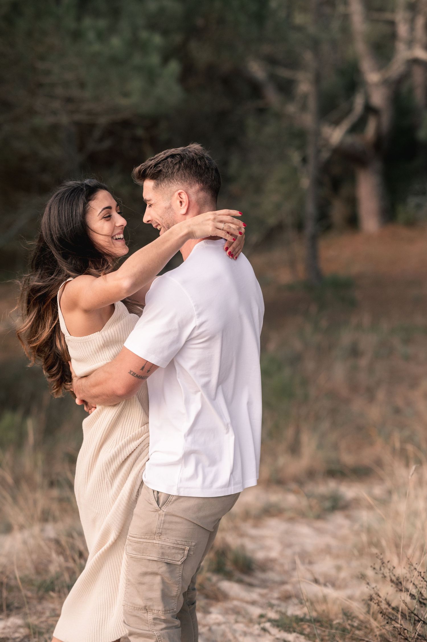 A romantic couple embraces in a natural outdoor setting with soft lighting and neutral tones.