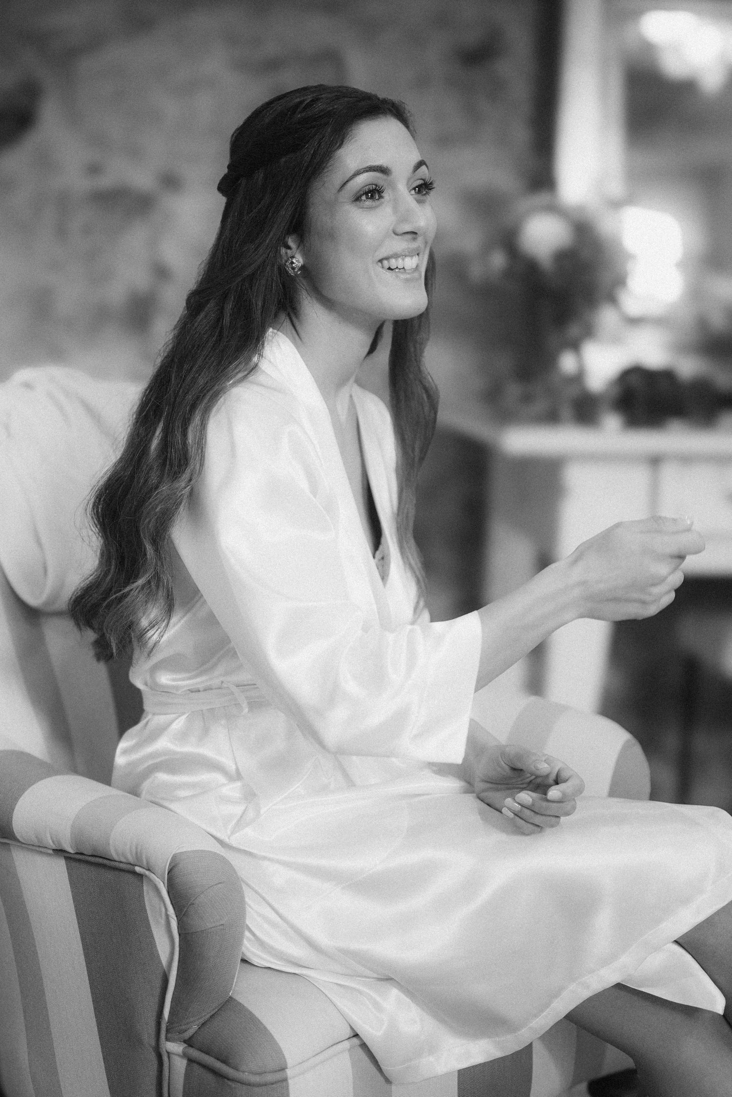 Black and white photo of person in white robe smiling while getting ready on wedding day morning.