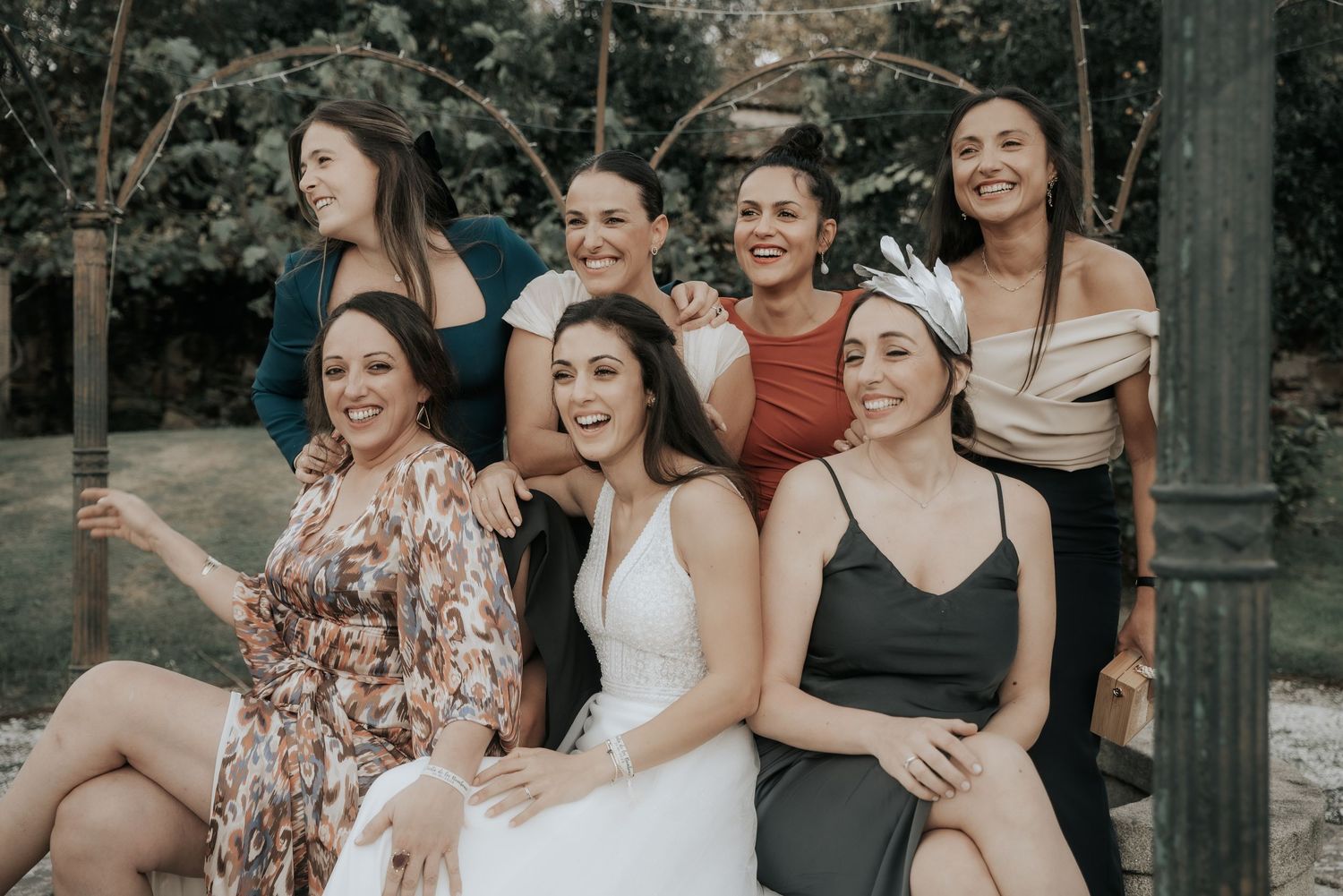 A group of friends in formal attire share joyful moments together during an outdoor celebration.