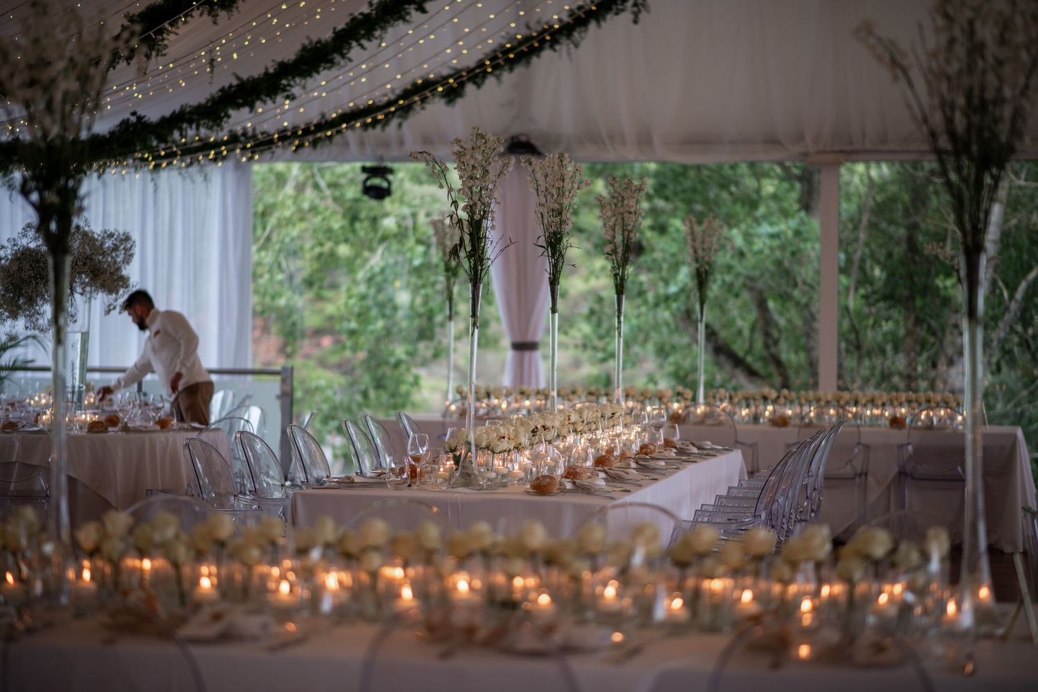 Outdoor wedding reception setup with twinkling string lights creating a romantic ambiance among trees.