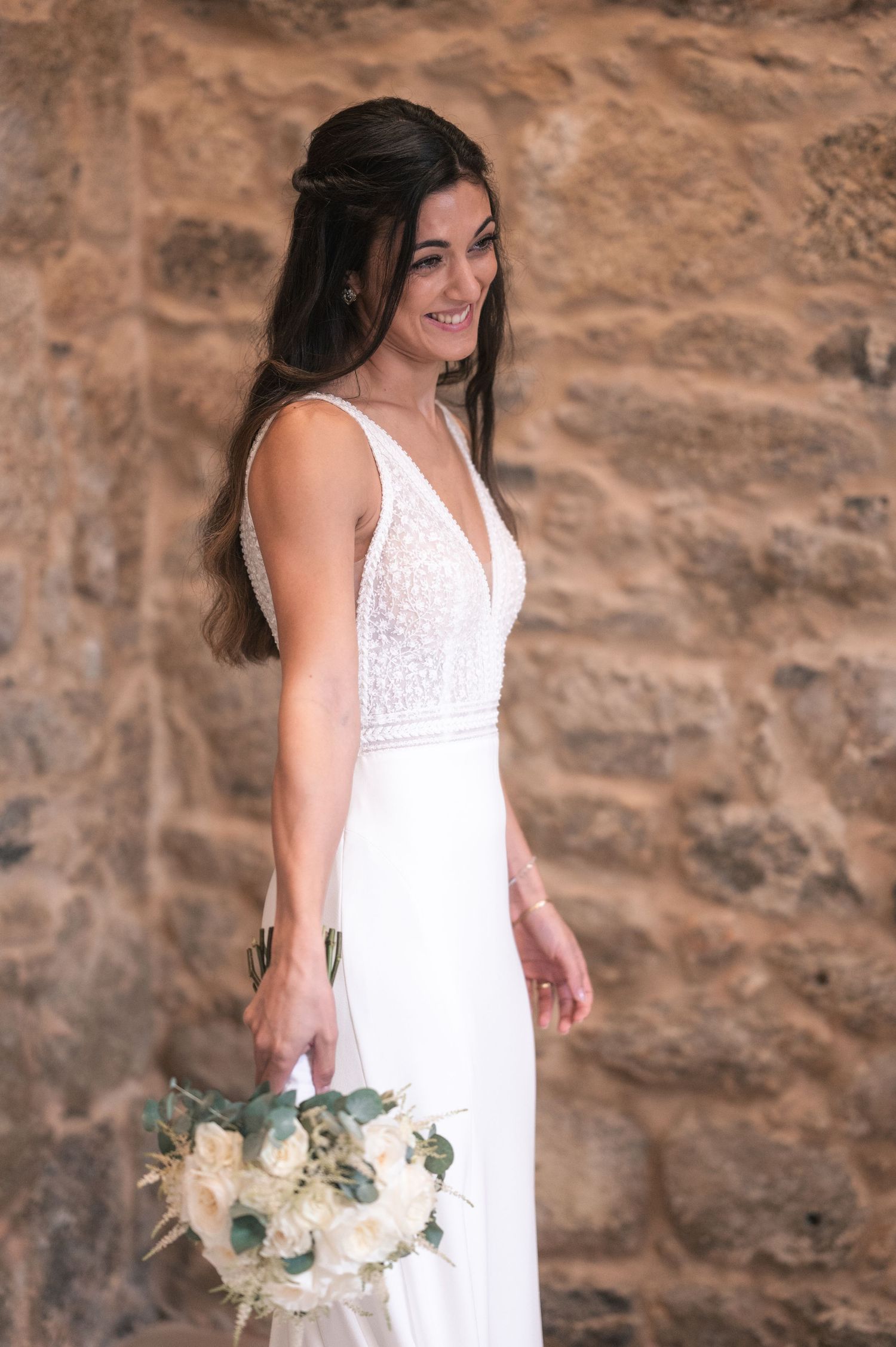 Elegant bridal portraits with white floral bouquet against textured stone backdrop.
