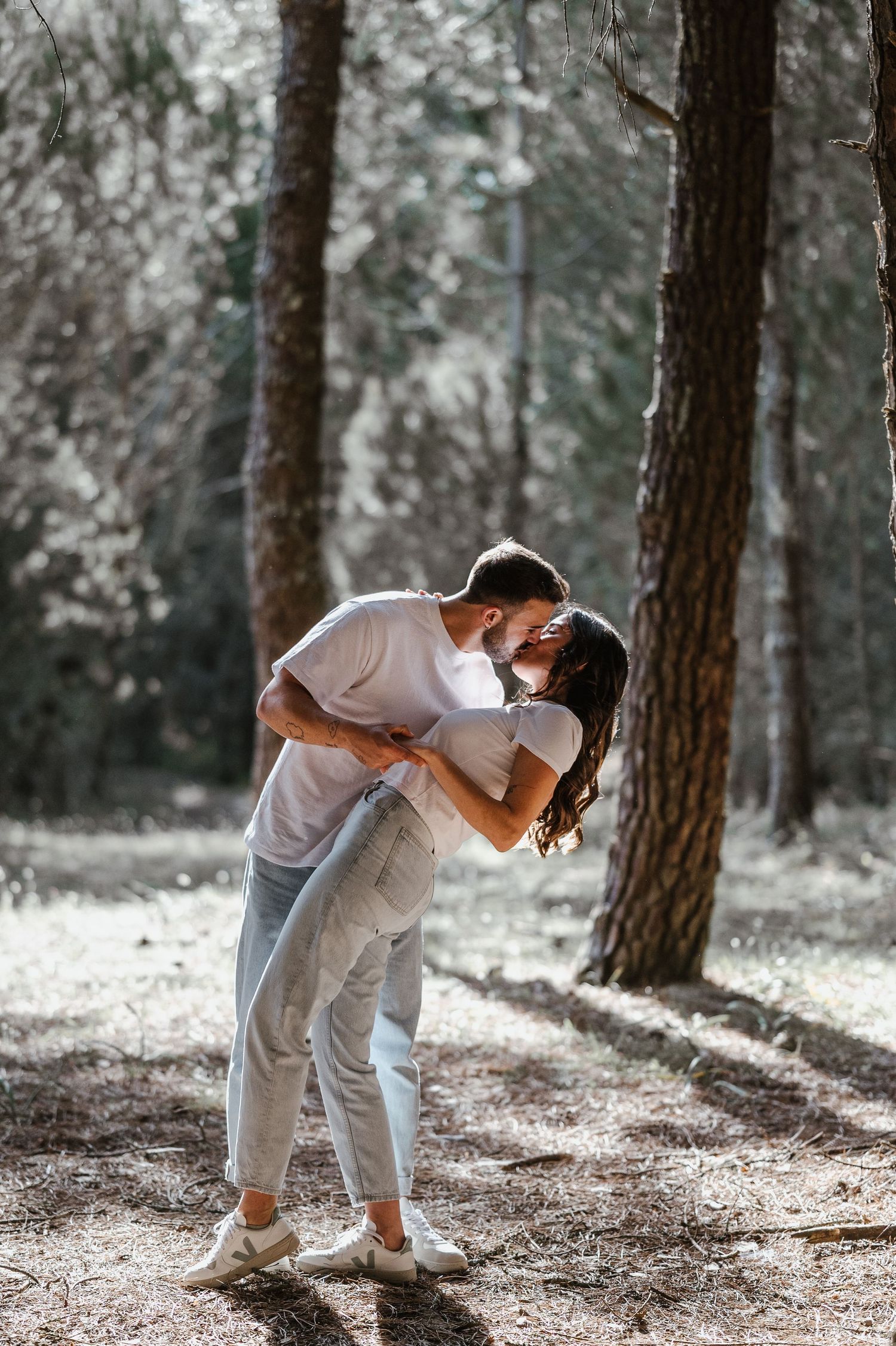 A romantic couple sharing an intimate moment while embracing in a sunlit forest setting.