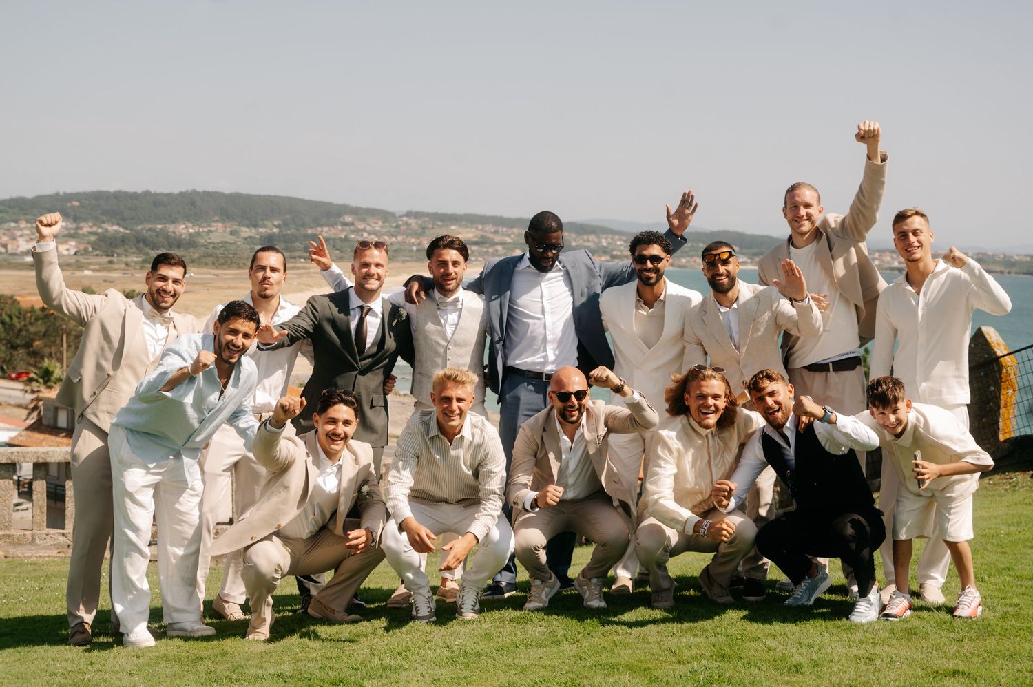 Cricket team members in white uniforms pose together on grass field during sunny day.