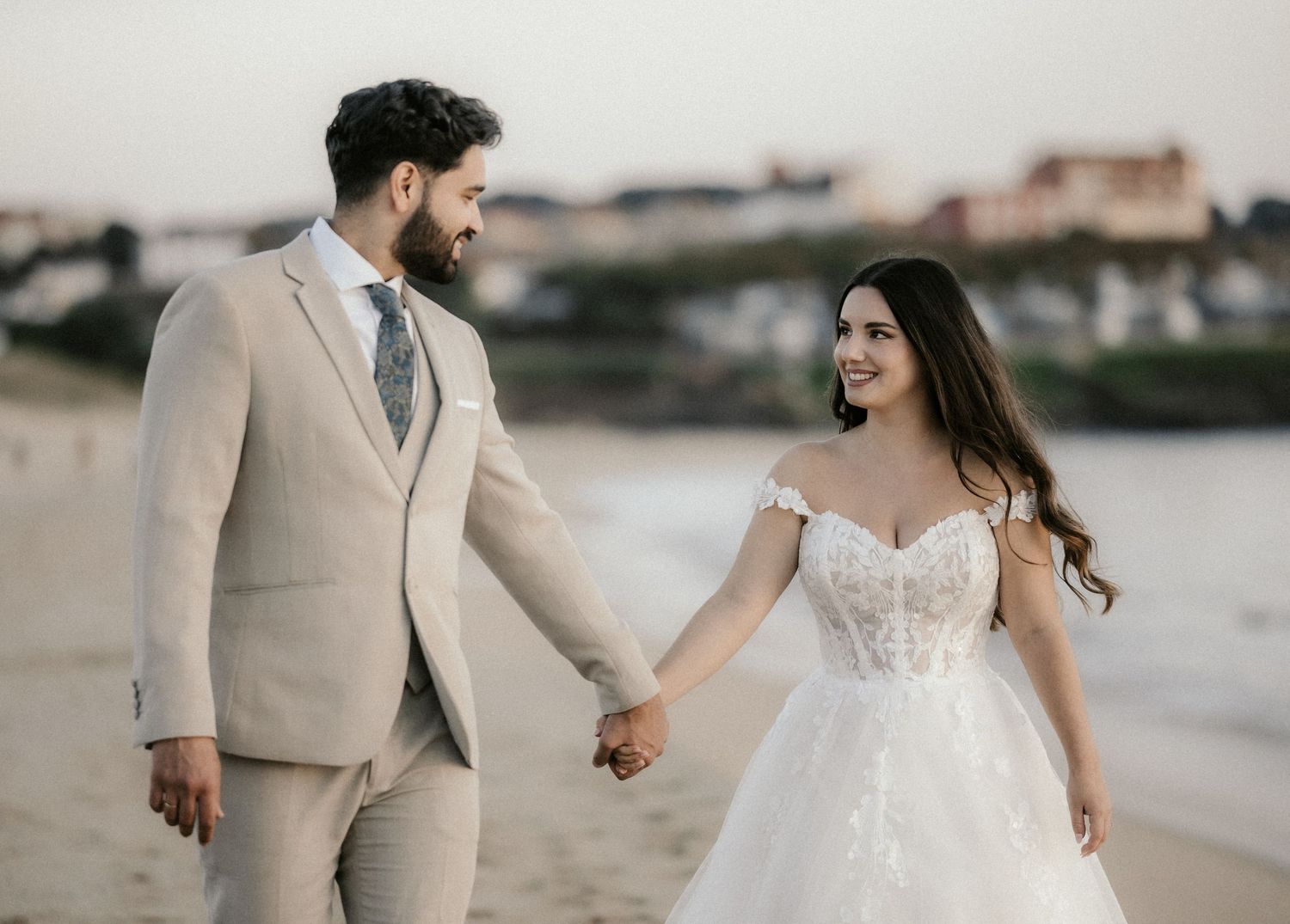 A beachside wedding photoshoot with a couple in elegant attire walking and dancing by the water.