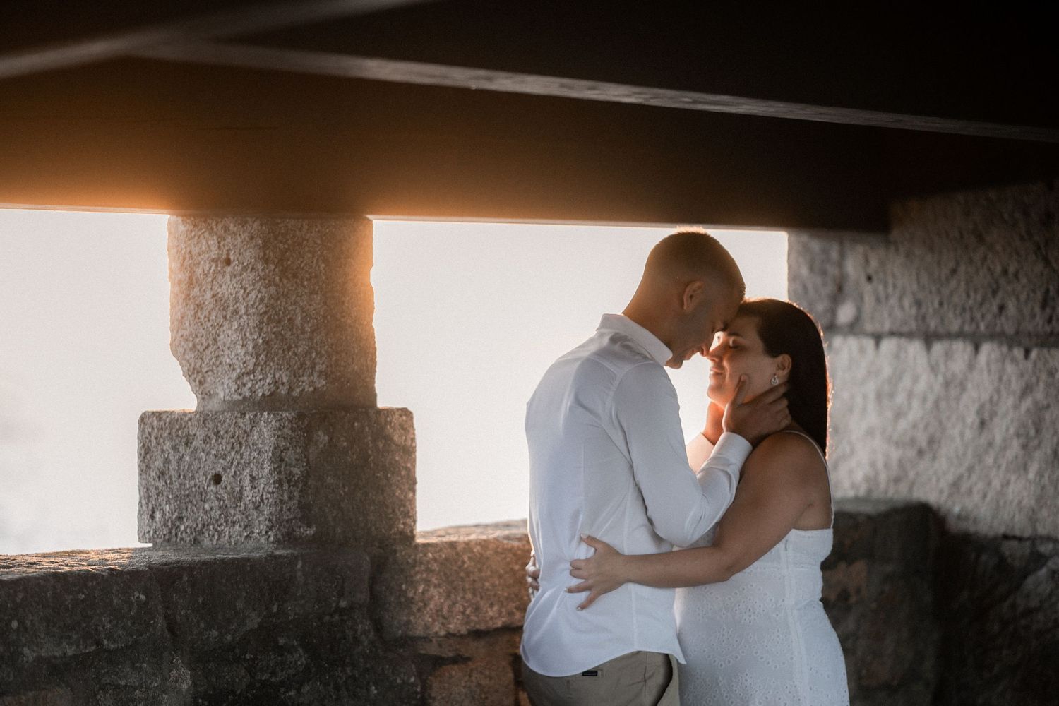 A couple embraces in silhouette against a bright window in a rustic indoor setting.