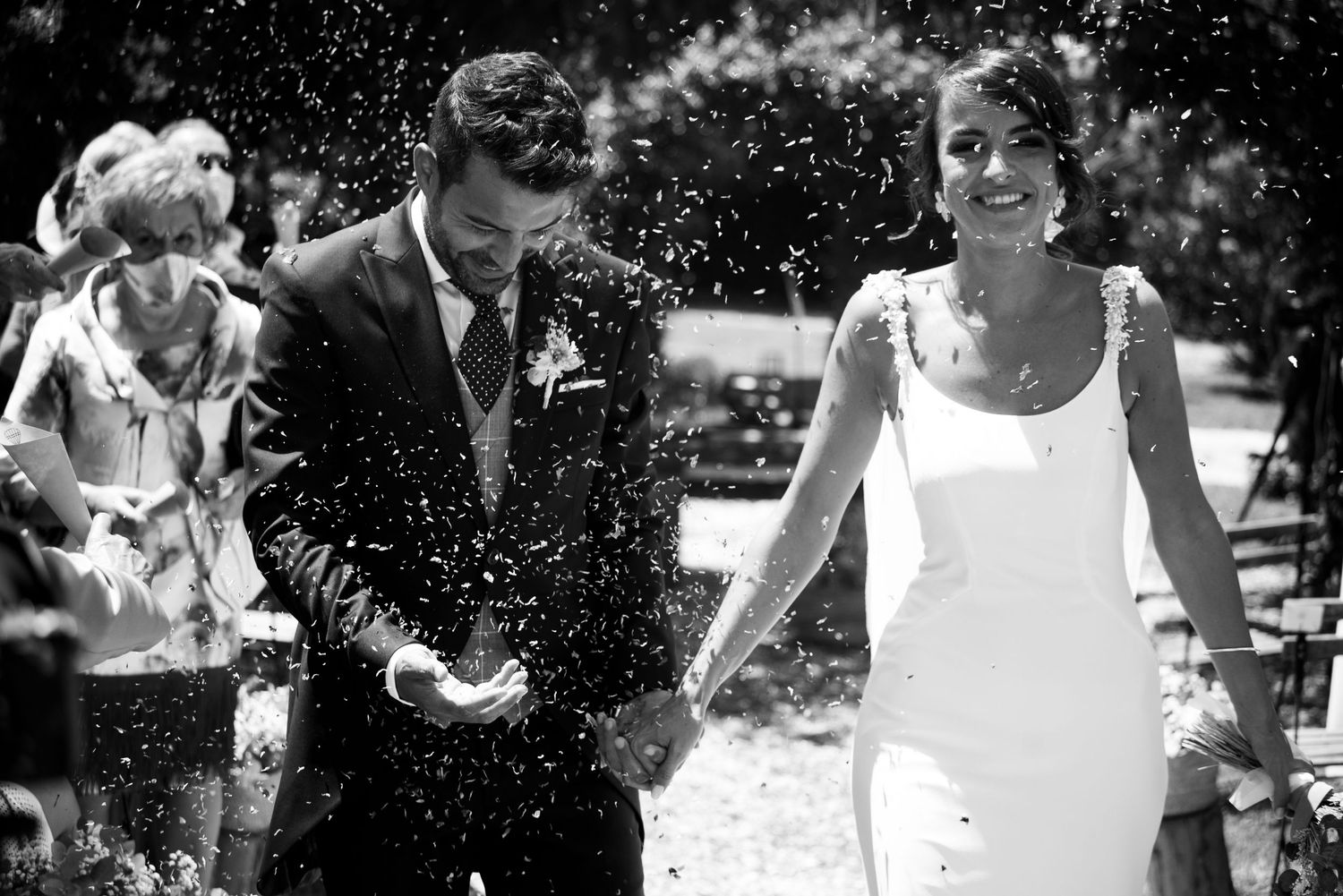 Wedding guests shower the newlyweds with confetti during an outdoor celebration.