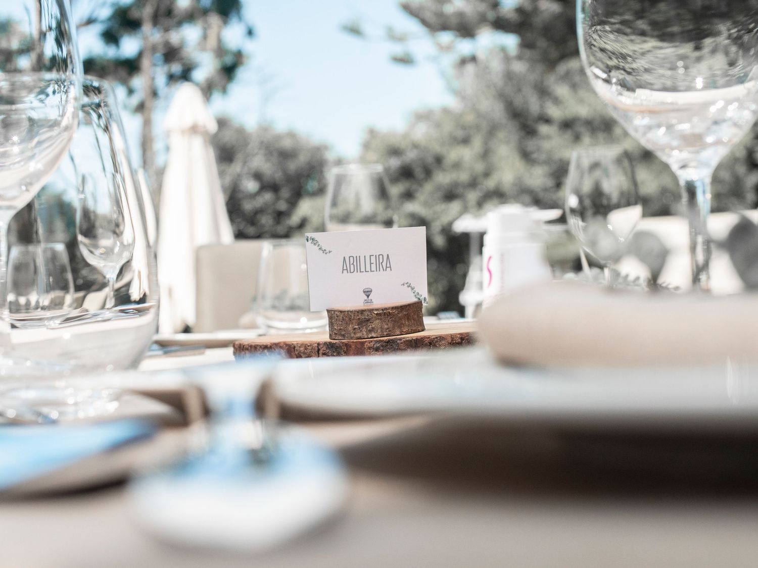 An elegant table setting with wine glasses and place cards at an outdoor restaurant in soft, muted tones.