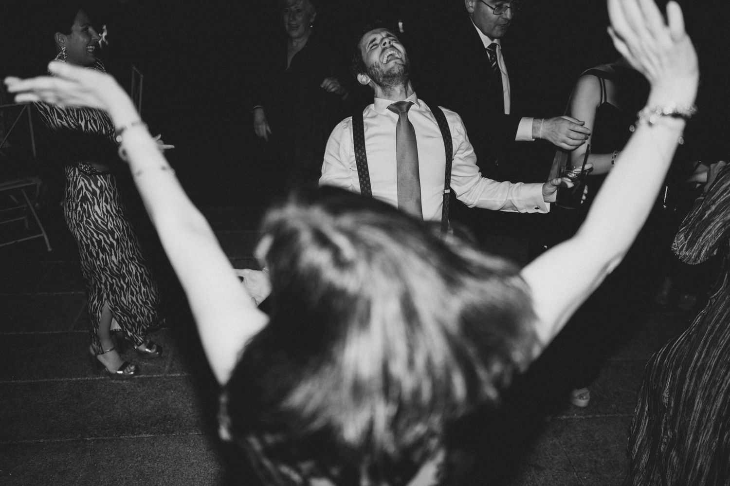 Black and white photo showing people dancing with raised arms at a lively party or celebration.