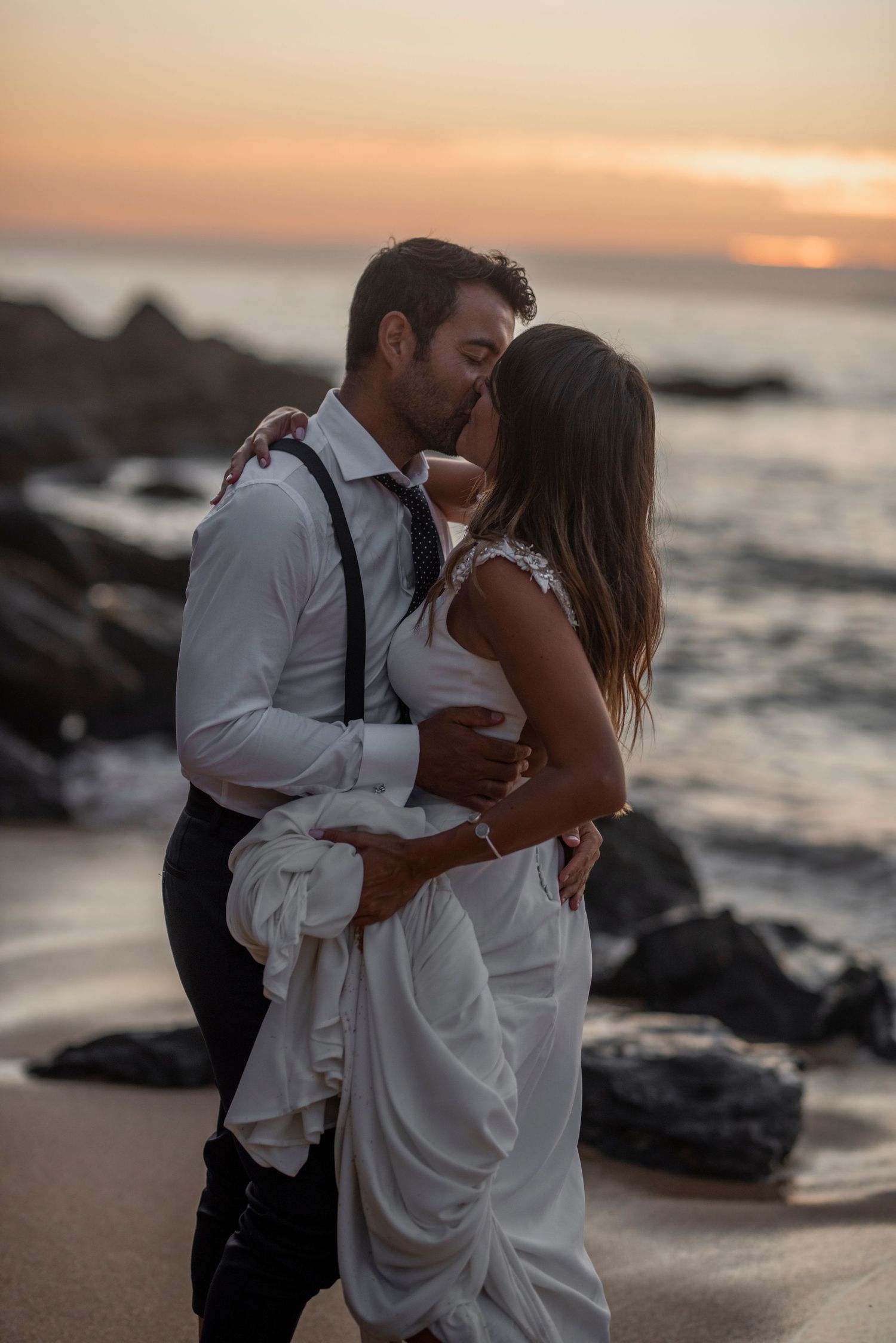 A romantic beach scene with a couple in formal wear sharing an intimate moment at sunset.