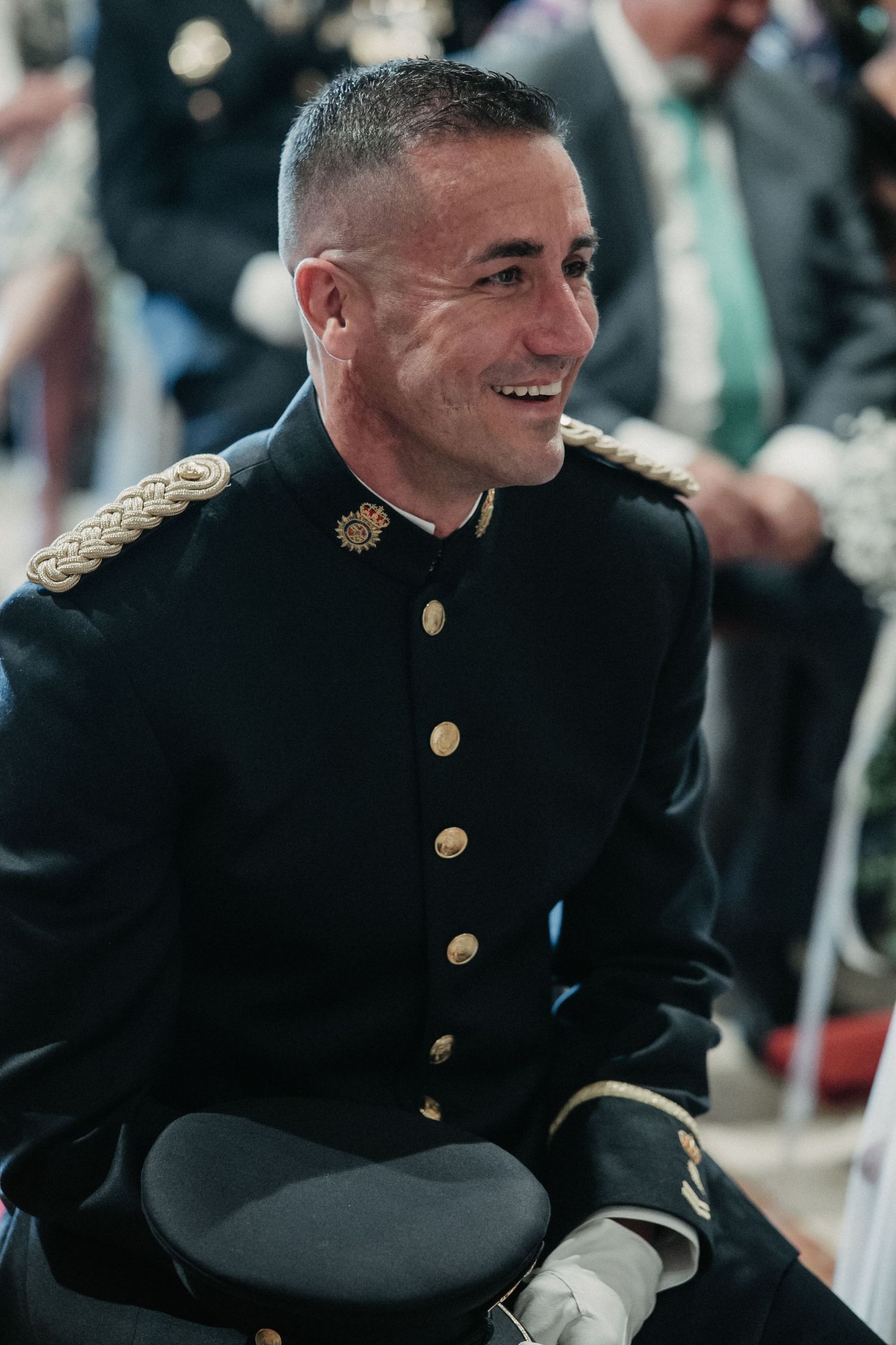 Service member in formal military dress uniform with gold buttons and epaulettes smiles during ceremony.