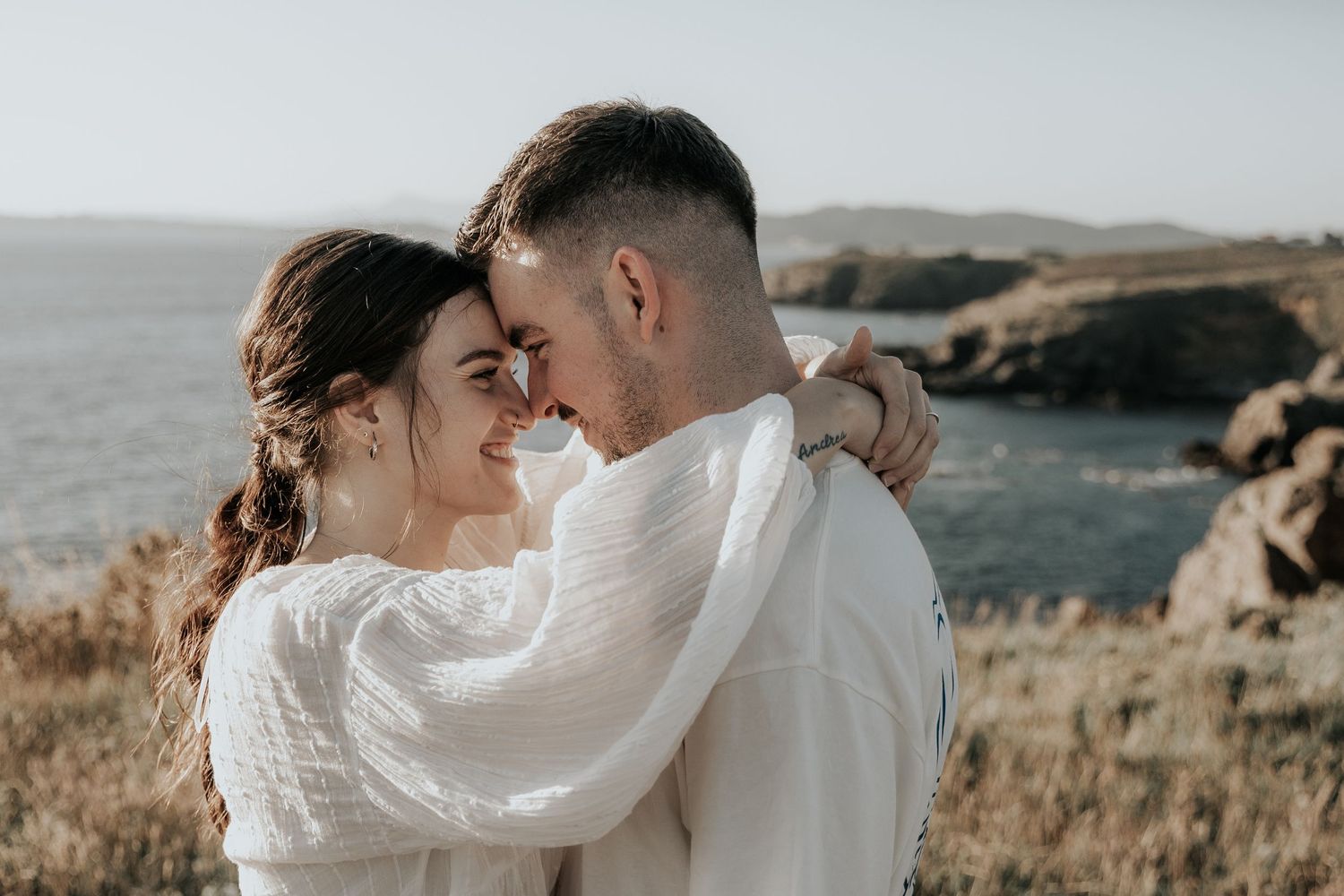 A couple shares an intimate moment against a scenic coastal backdrop during sunset.